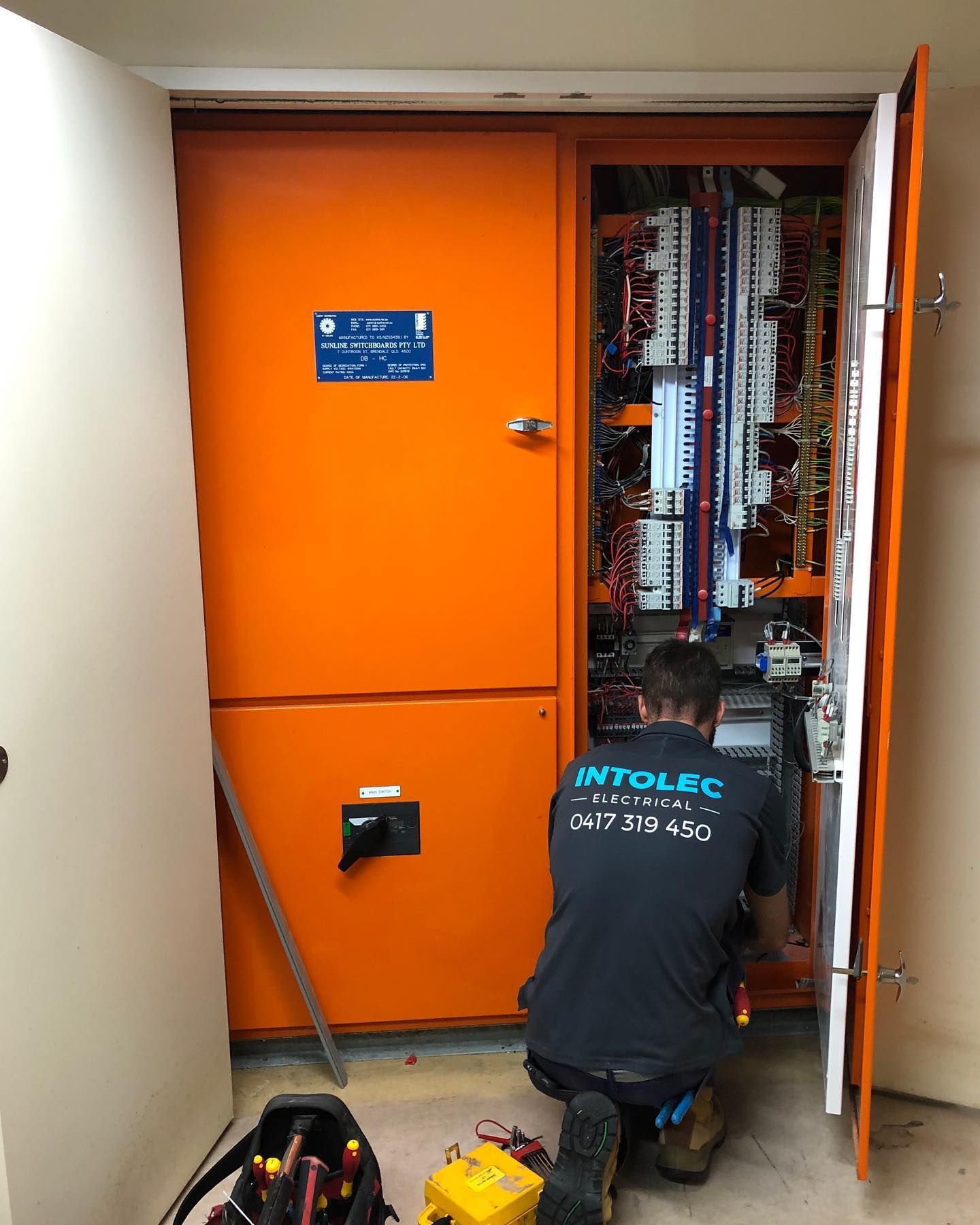 Electrician working on an orange electrical panel inside a room. The panel's door is open. — Intolec Electrical In Tweed Heads, NSW