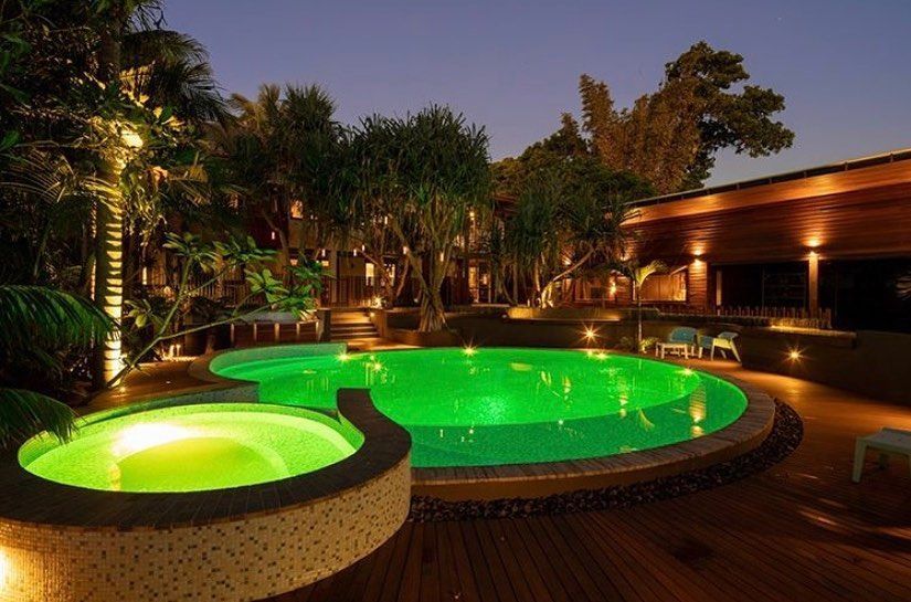Nighttime view of a glowing green pool and hot tub surrounded by trees and wooden deck, at a resort. — Intolec Electrical In Tweed Heads, NSW