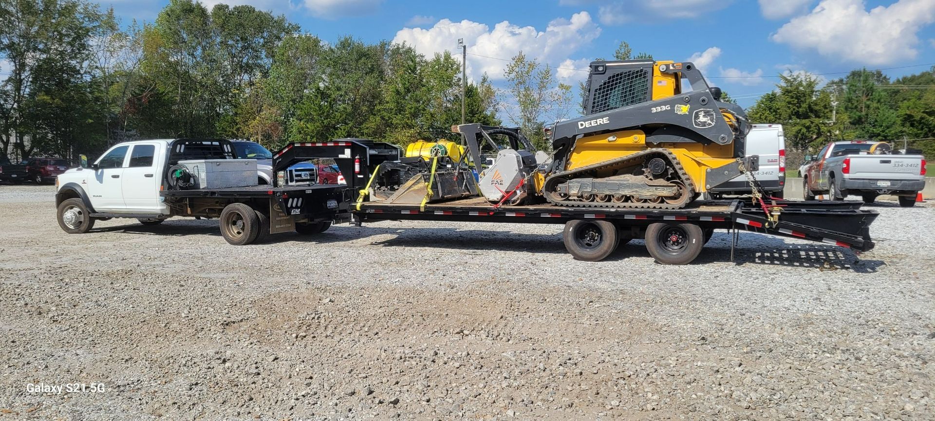 Tow truck hauling a yellow excavator and two vehicles on a flatbed trailer in a gravel lot.