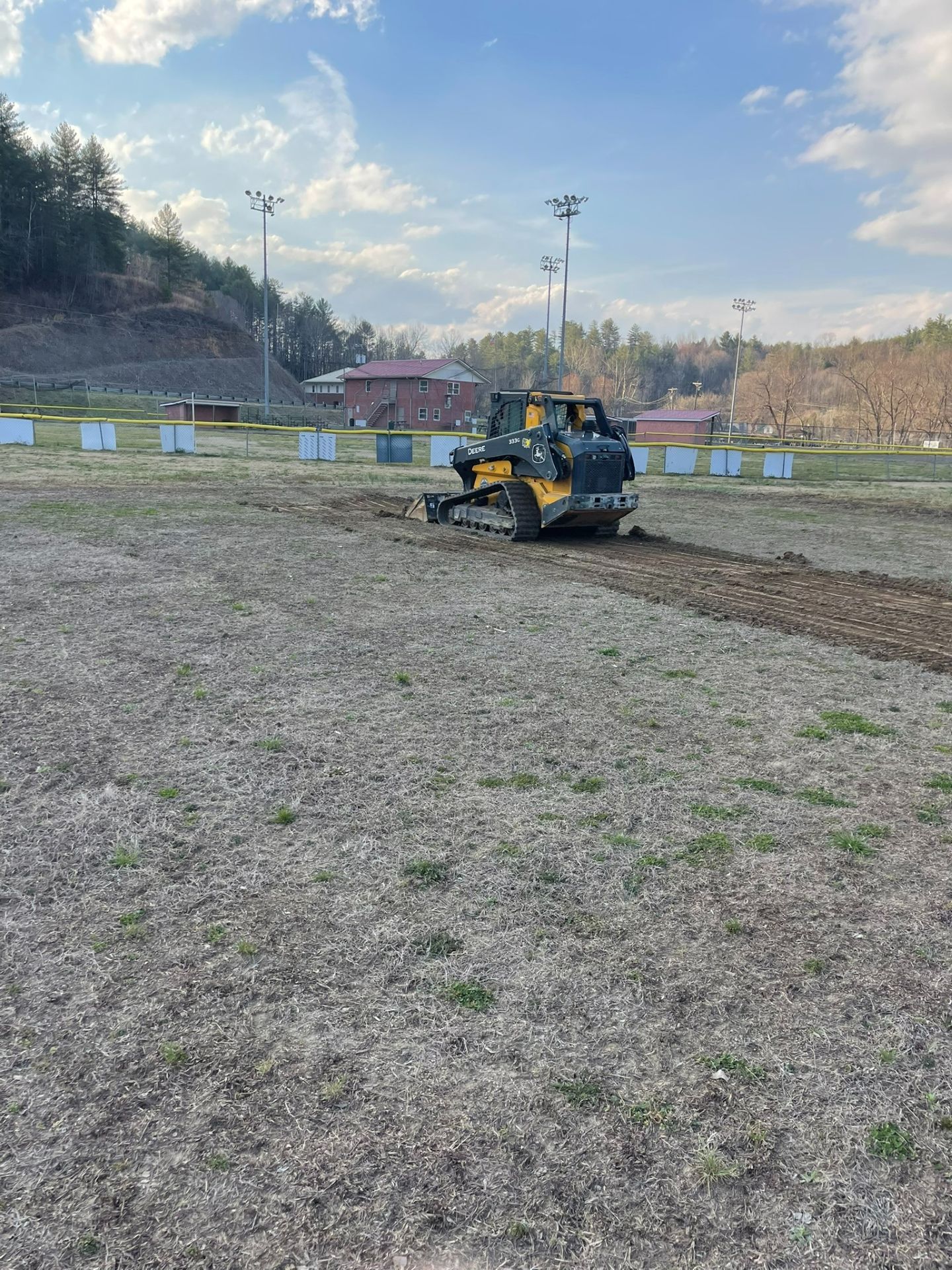 Yellow construction vehicle leveling dirt on a grassy field under a blue sky