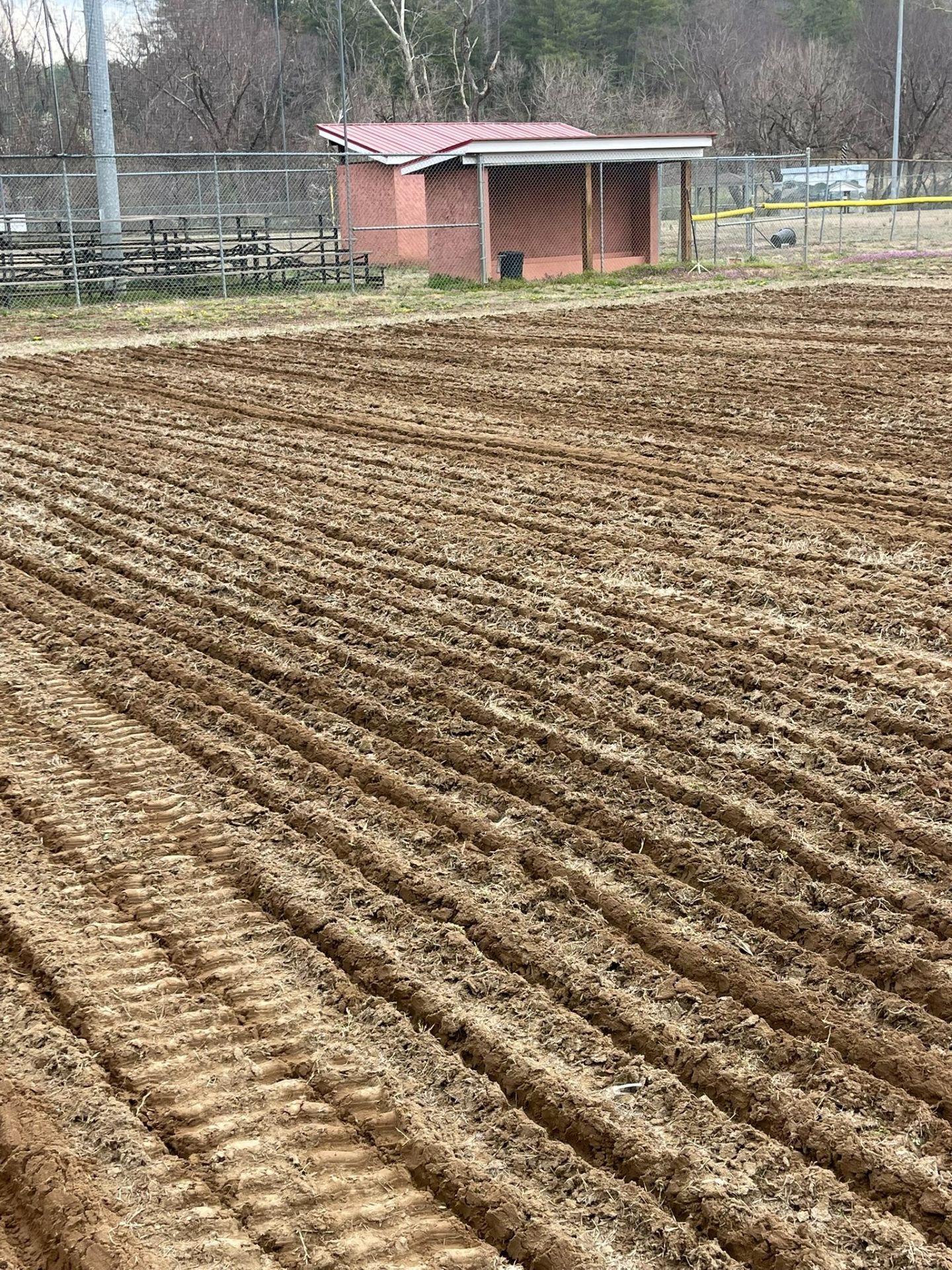 Plowed field with rows of soil and a small red shed in the background.