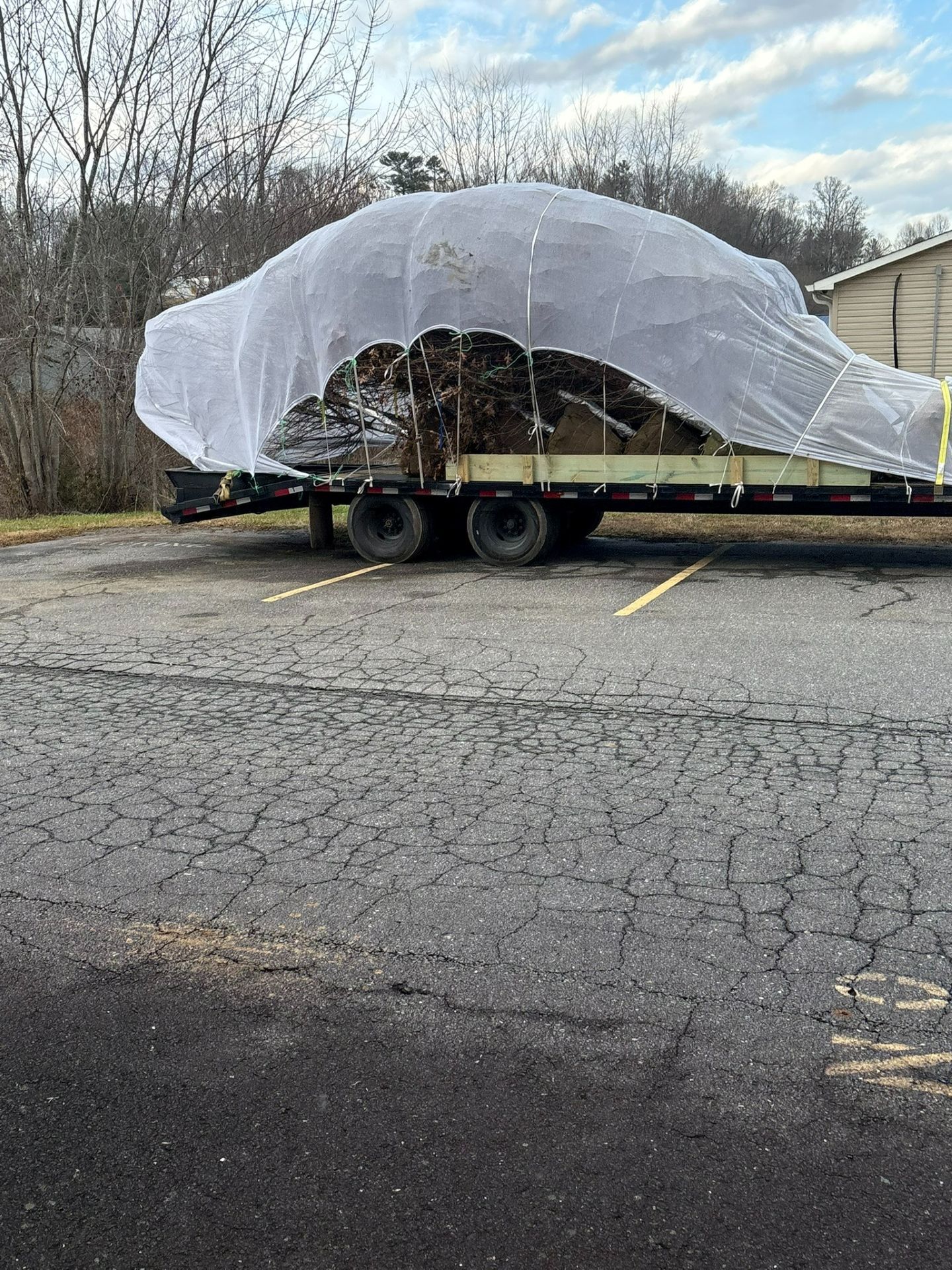 Flatbed trailer carrying a large, tarp-covered load in an empty parking lot under cloudy skies