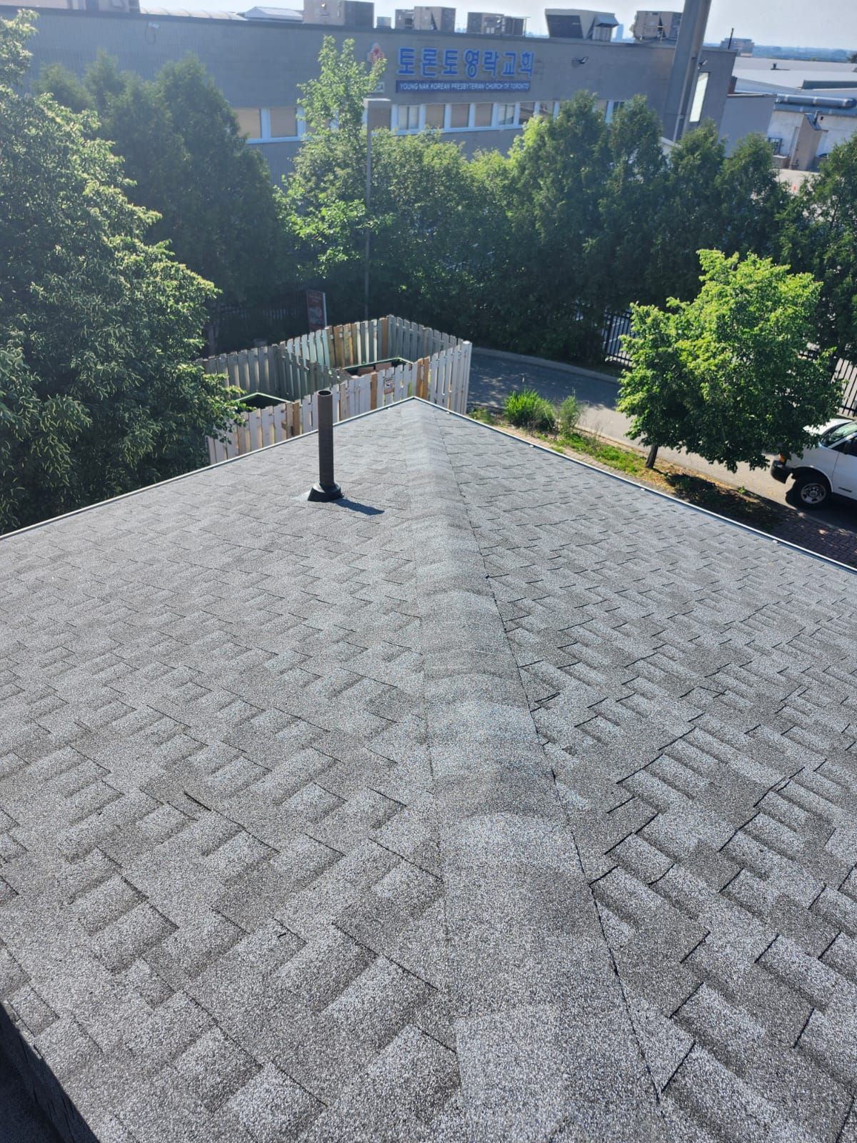 Rooftop with gray shingles, chimney vent, and trees and buildings in the background