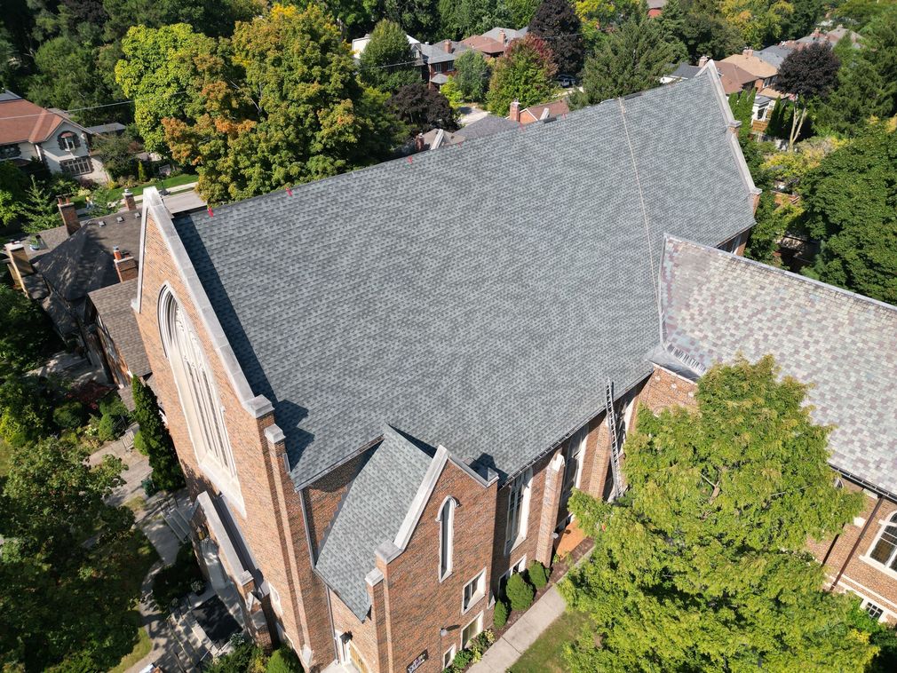 Aerial view of a brick church with a gray roof surrounded by trees and neighboring buildings