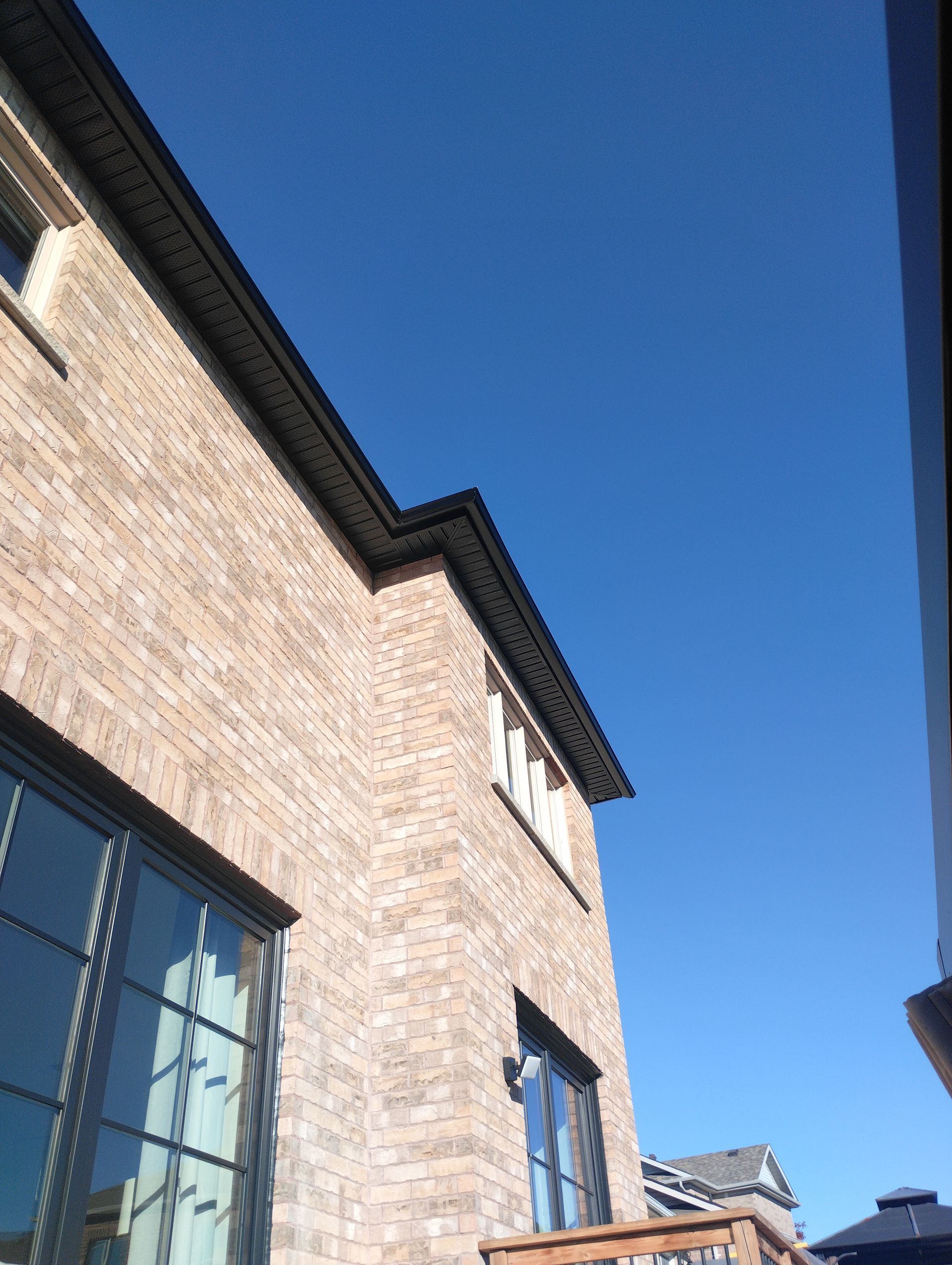 A multi-story brick house with a dark roof against a clear, deep blue sky.