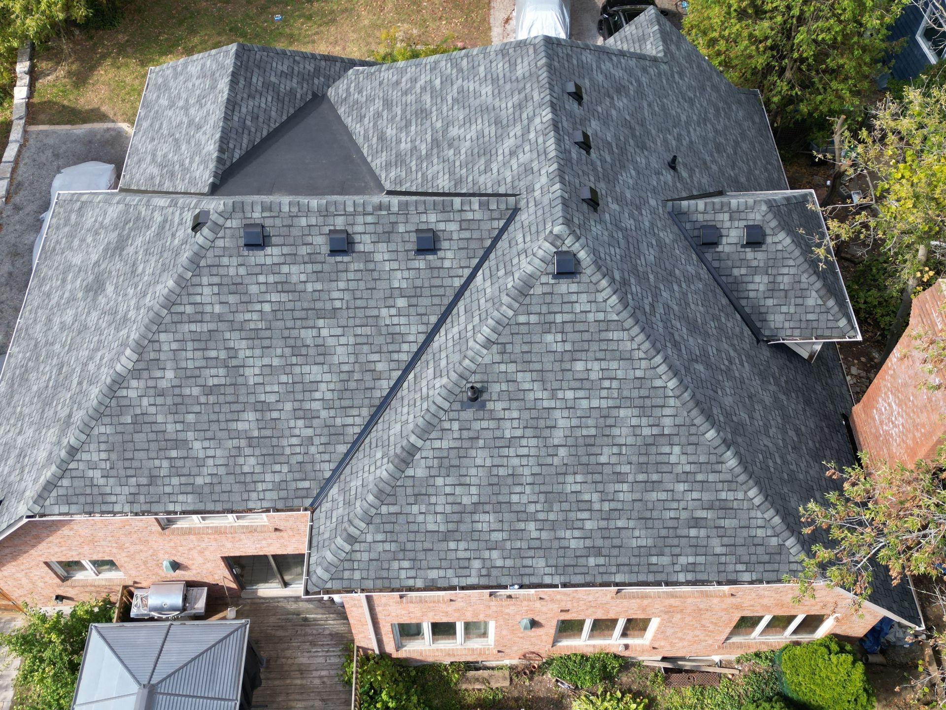 Aerial view of a brick house with a dark gray shingled roof and skylights.
