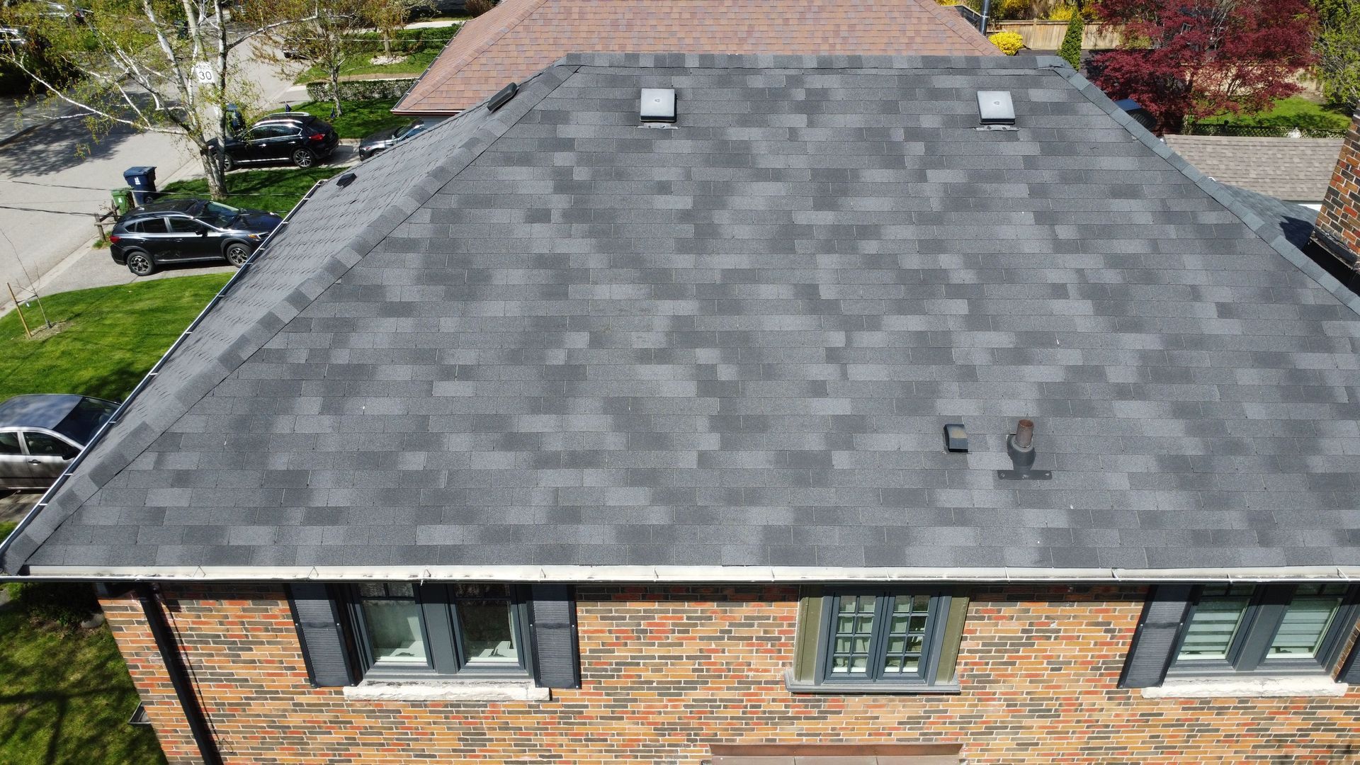 Aerial view of a house roof with dark gray shingles and two vent pipes.