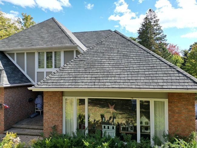 Brick house with gray shingled roof and large front window under a blue sky