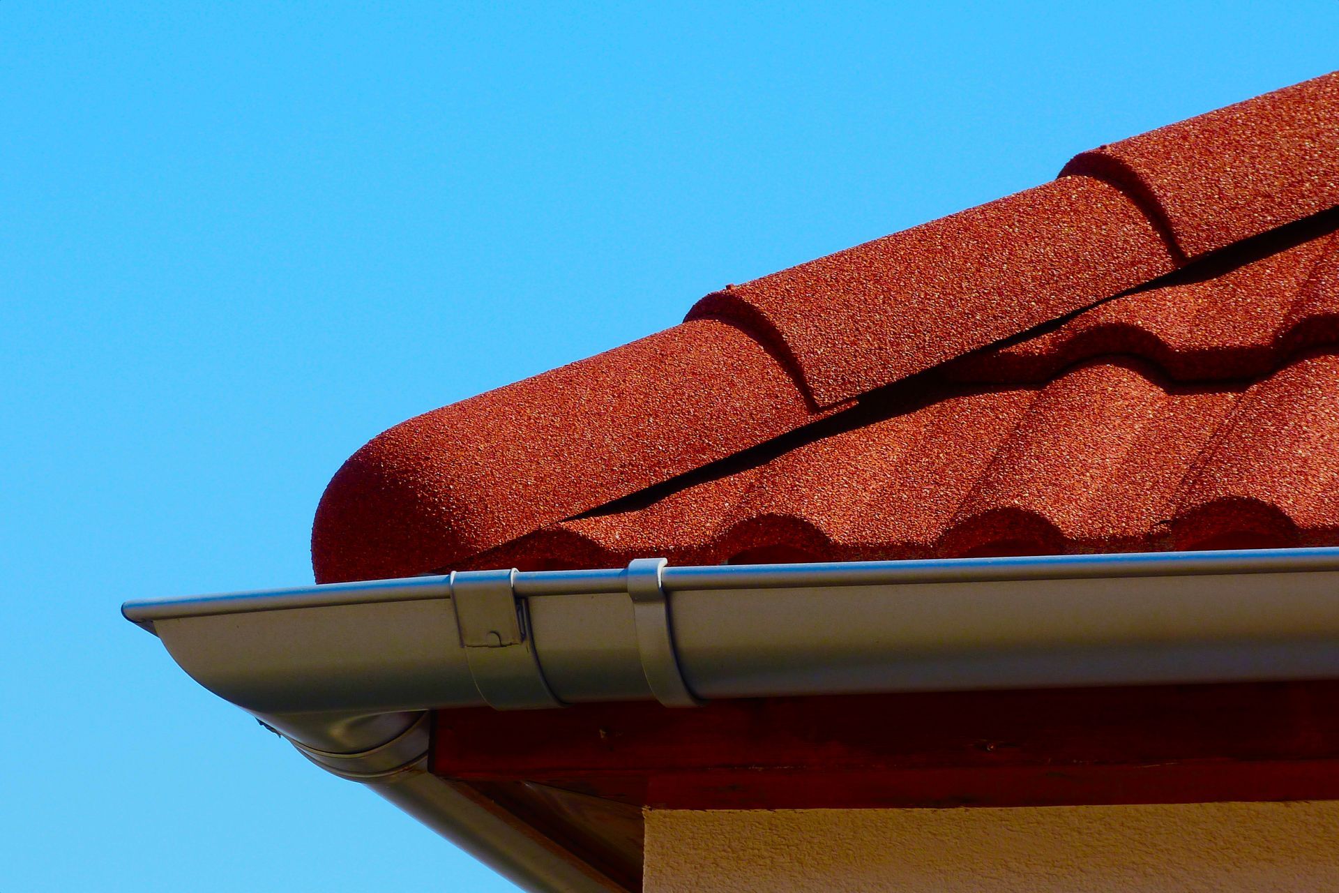 Red tiled roof and silver gutter against a clear blue sky.