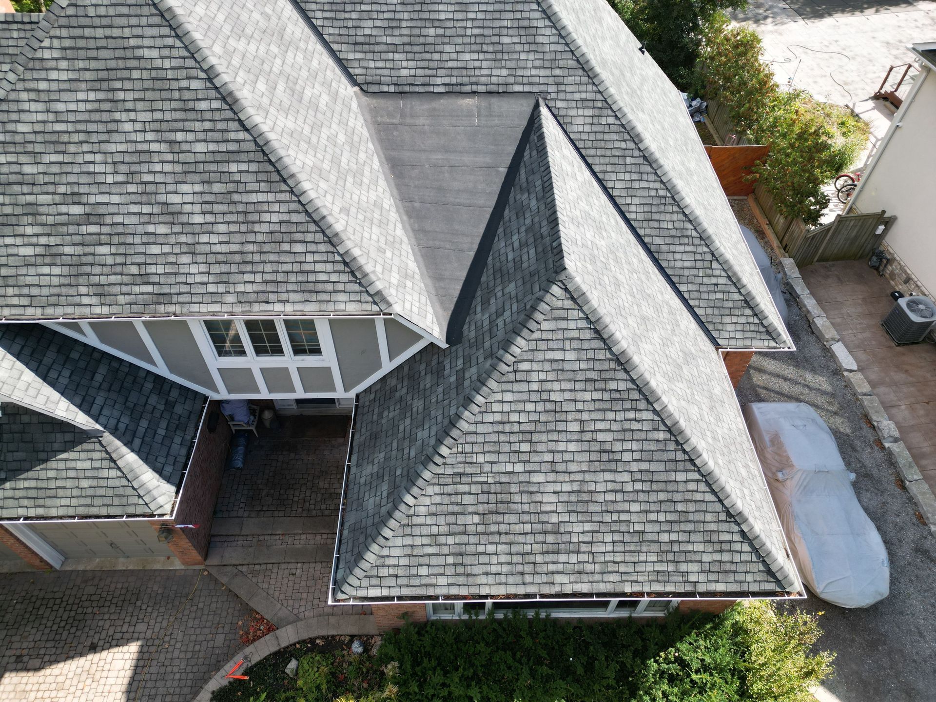 Aerial view of a gray-shingled house roof with multiple gables and a driveway beside it
