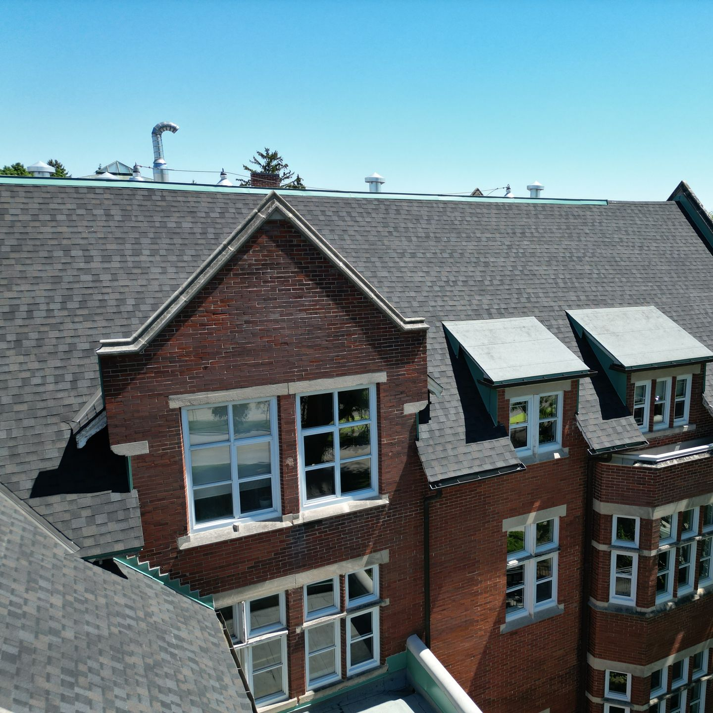 Red brick residential building with gray shingled roofs and white-framed windows under a blue sky