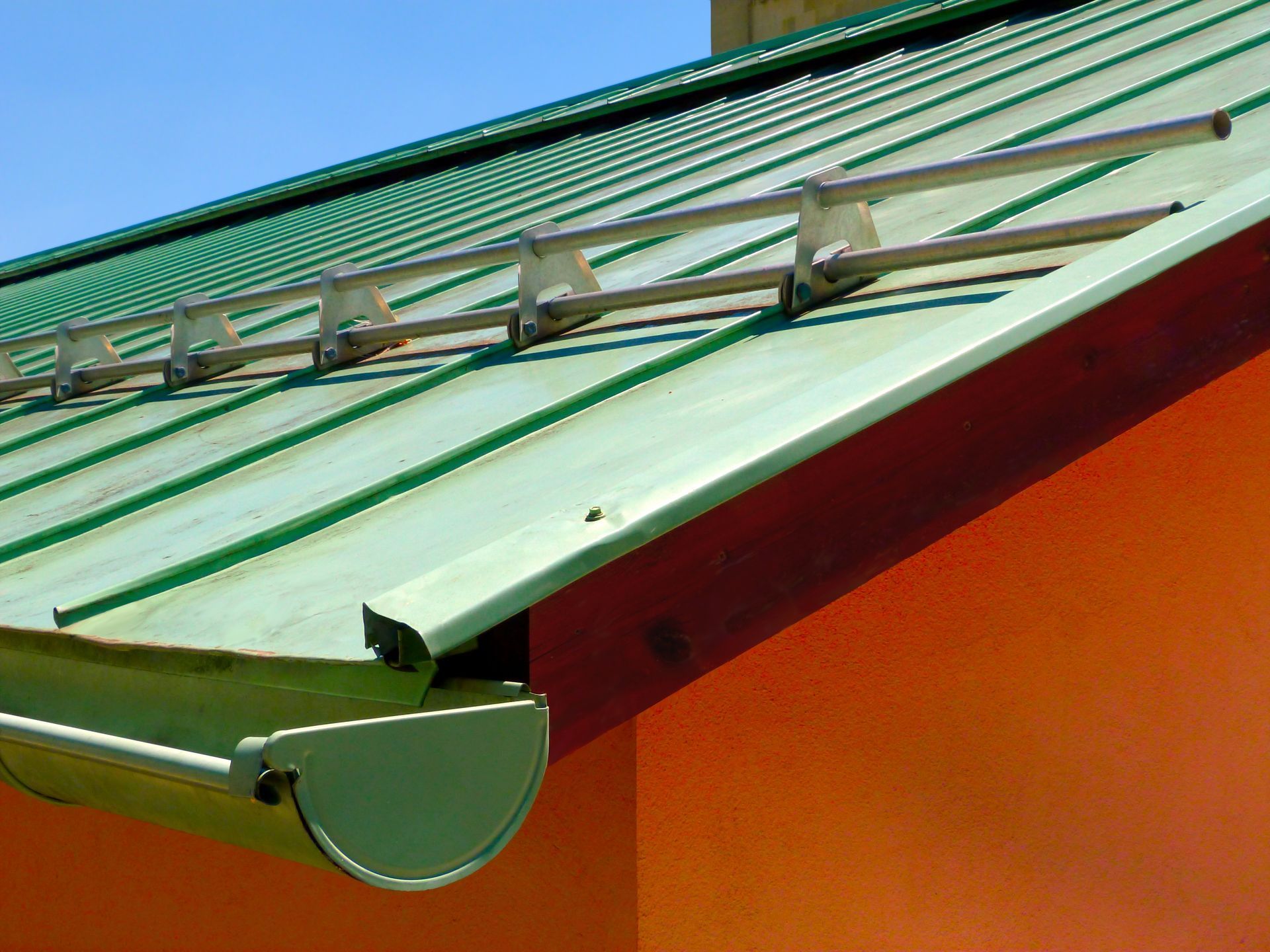 Green metal roof with an orange wall and a ladder on top