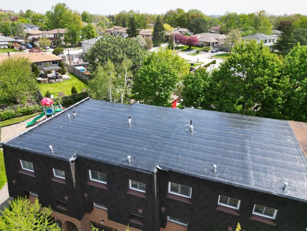Aerial view of a dark-roofed apartment building surrounded by green trees and neighboring houses