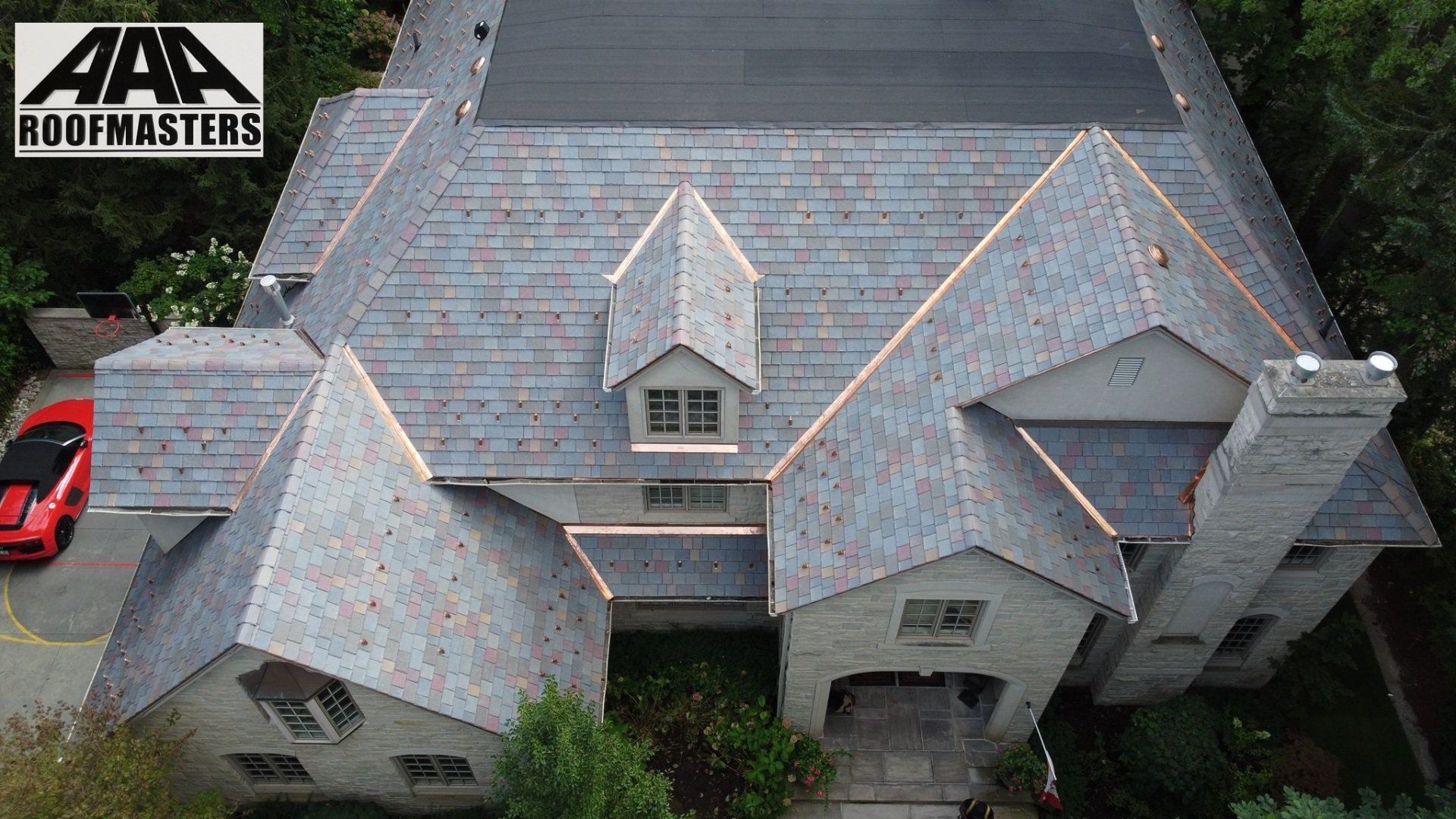 An aerial view of a large house with a red car parked in front of it.