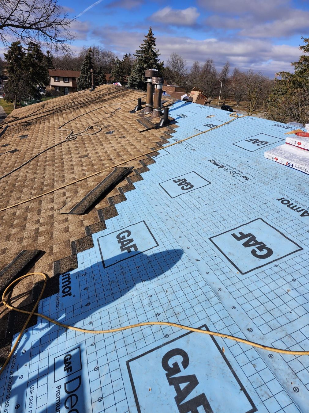 Roof under repair with blue underlayment on the right and exposed wood decking on the left