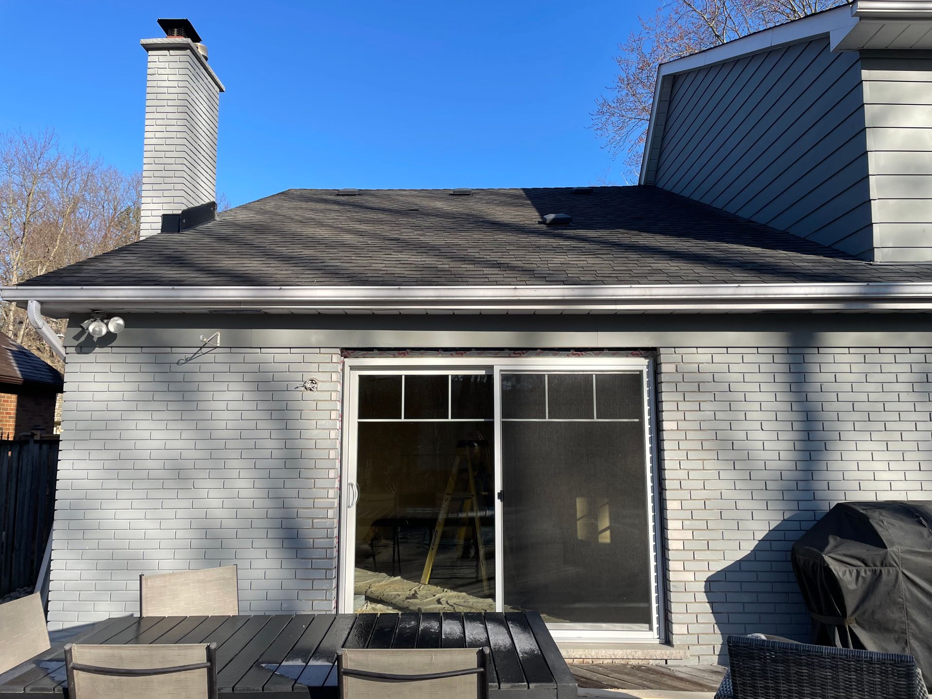 Back patio with white brick wall, sliding glass door, chimney, and a covered grill under a blue sky