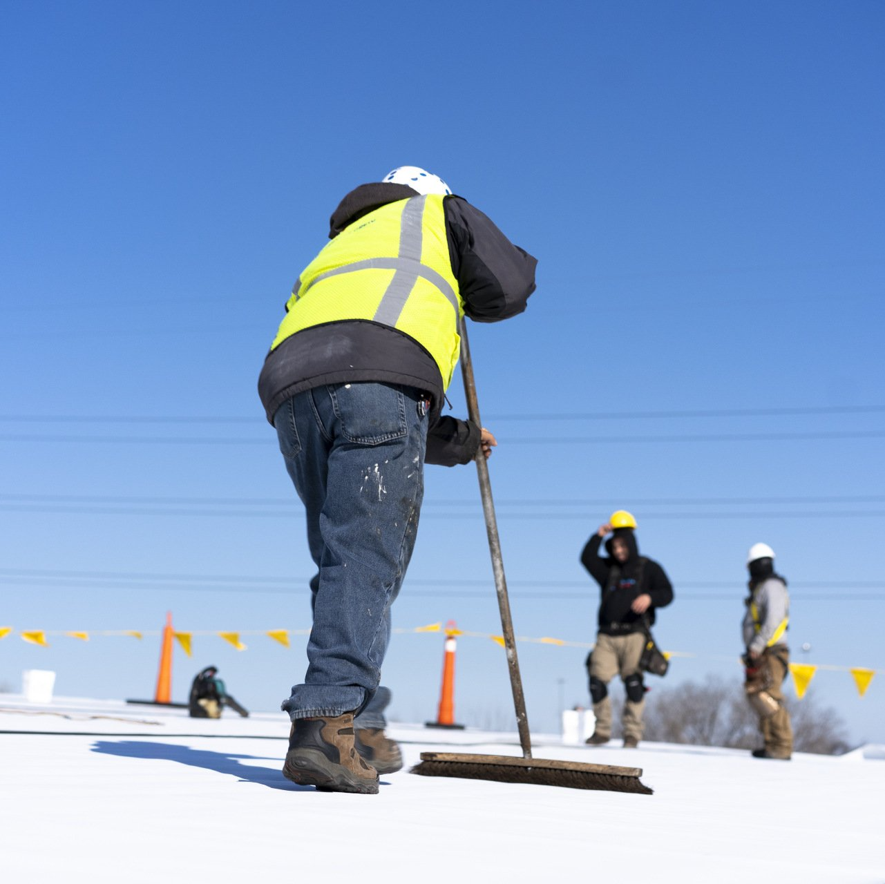 A man in a yellow vest is sweeping the snow