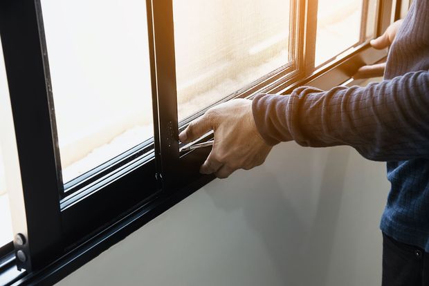 A person installing a black mesh screen into a sliding window frame.