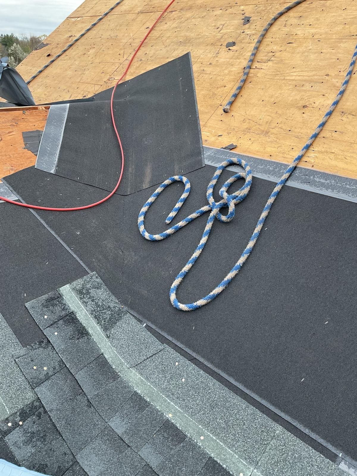 A roof under construction featuring exposed wood decking, black underlayment, installed shingles, and a coiled safety rope.