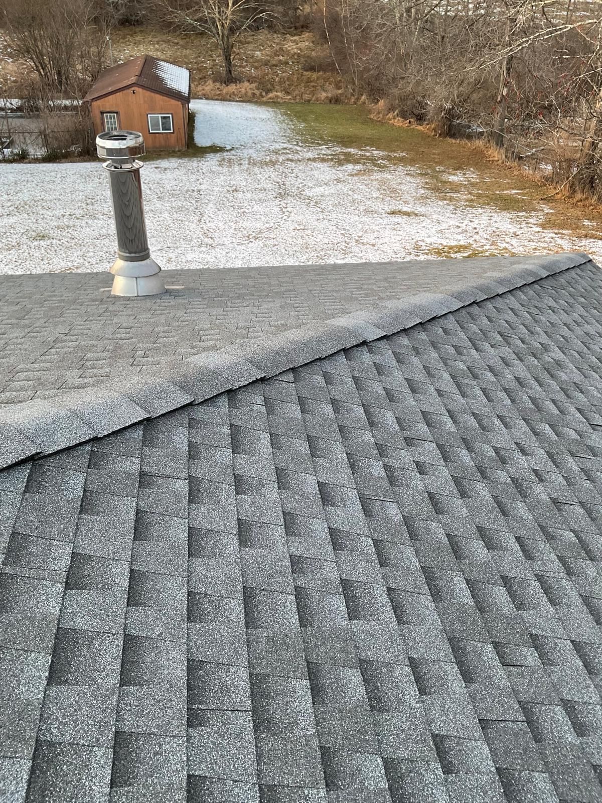 A view from a grey shingled roof looking down at a snow-dusted yard and a small brown shed.