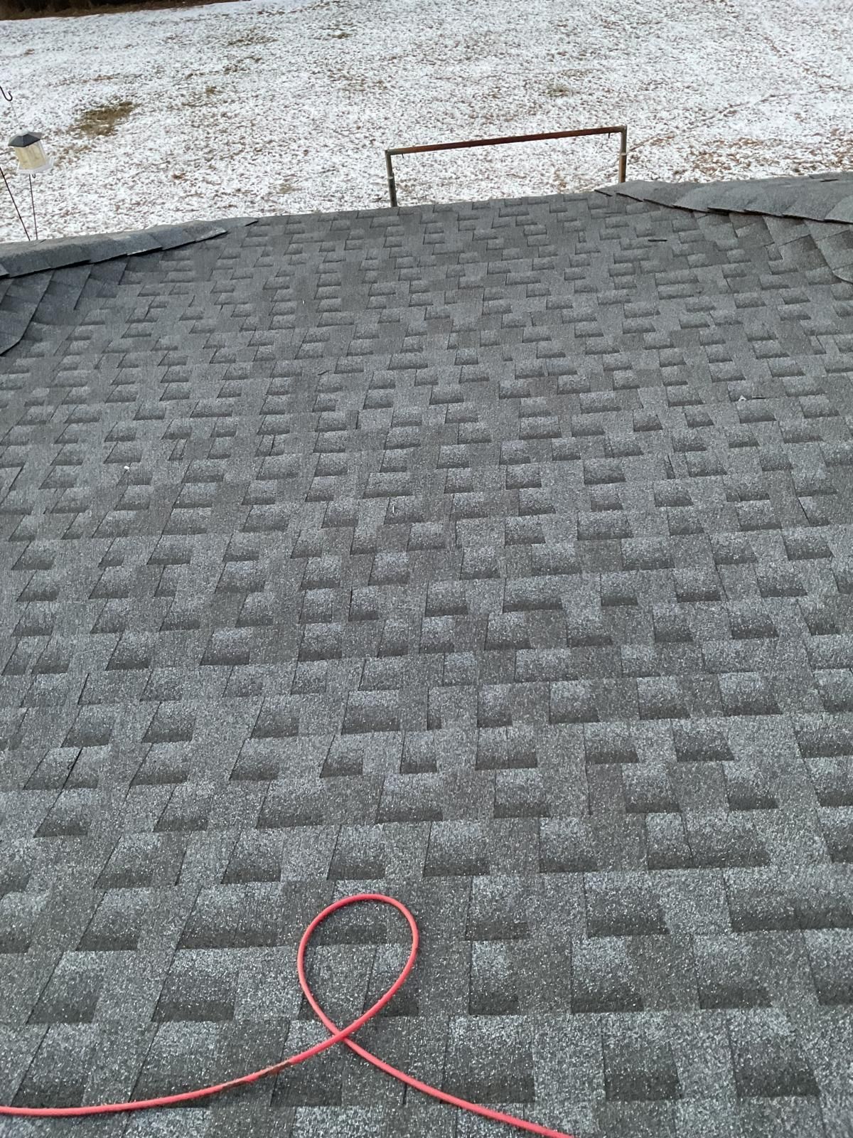 A textured, dark grey asphalt shingle roof, with a red cord laying across it and a metal frame visible in the distance.