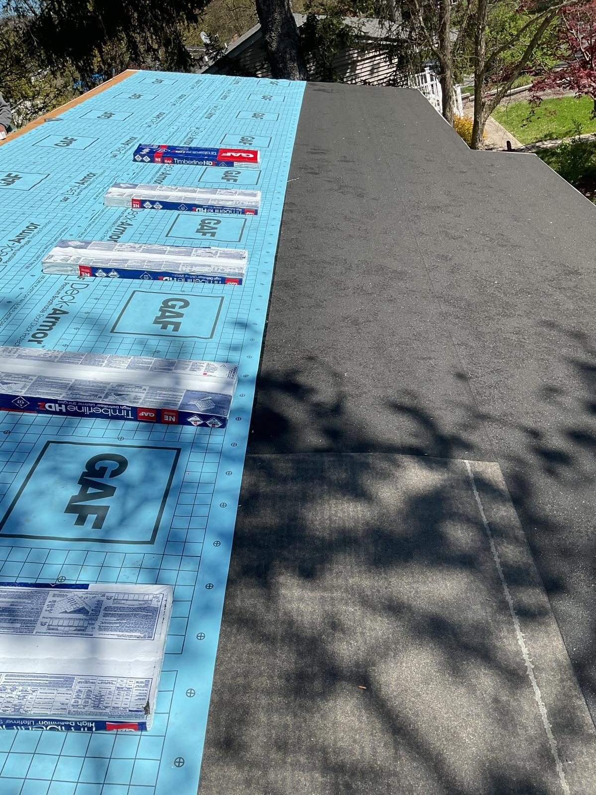 A view of a roof under renovation, showing dark shingles on the right and blue GAF underlayment installed on the left.