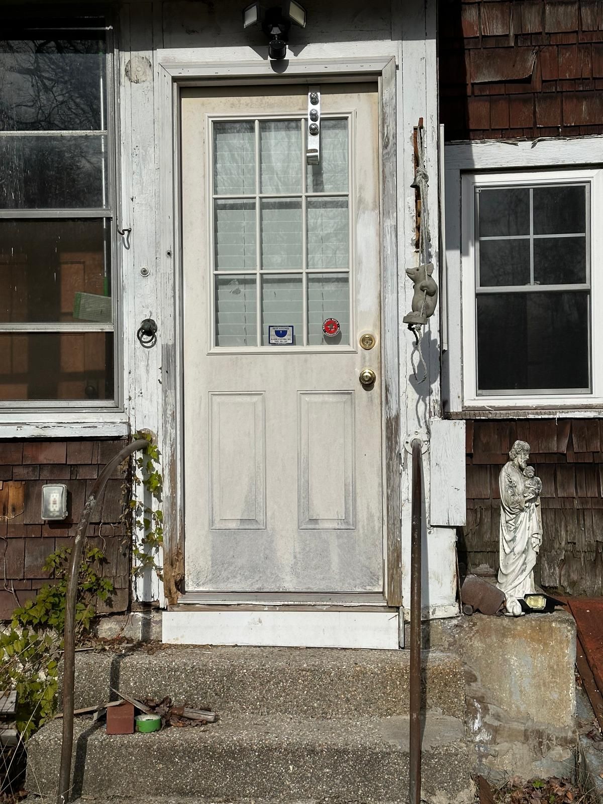 A weathered white door with a window and a small statue to its right, set in a house exterior with stone steps.