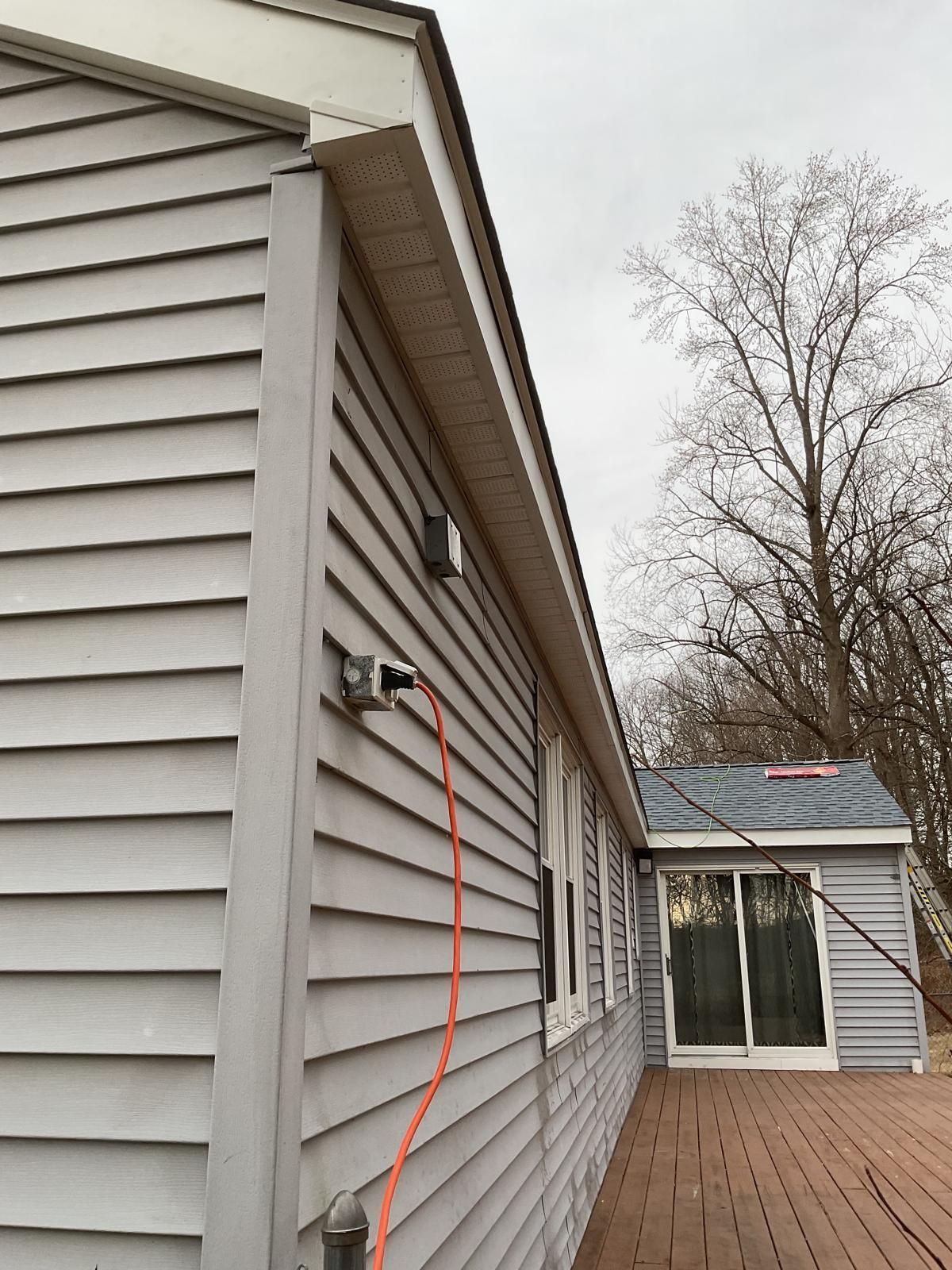 Gray vinyl siding on the side of a house featuring an outdoor electrical outlet with an orange extension cord plugged in.