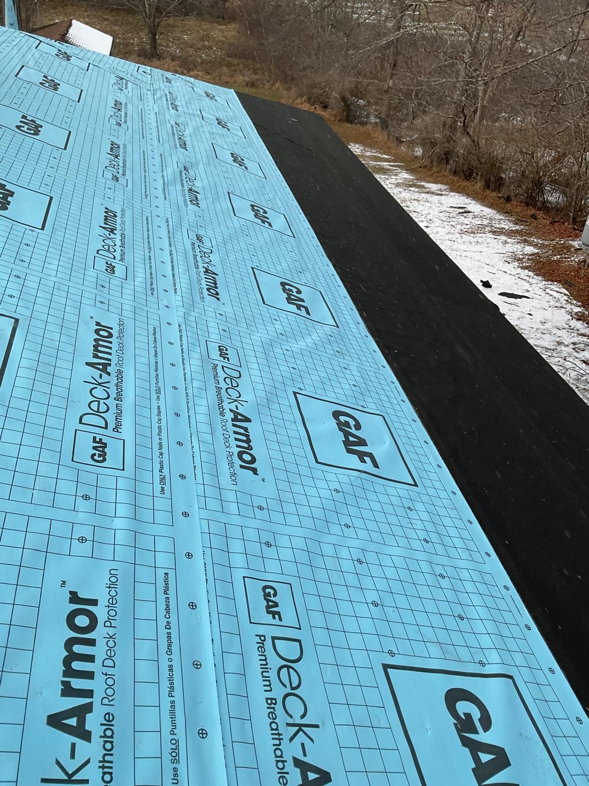 A view of a roof under construction, featuring blue GAF Deck-Armor underlayment installed over black roofing paper.