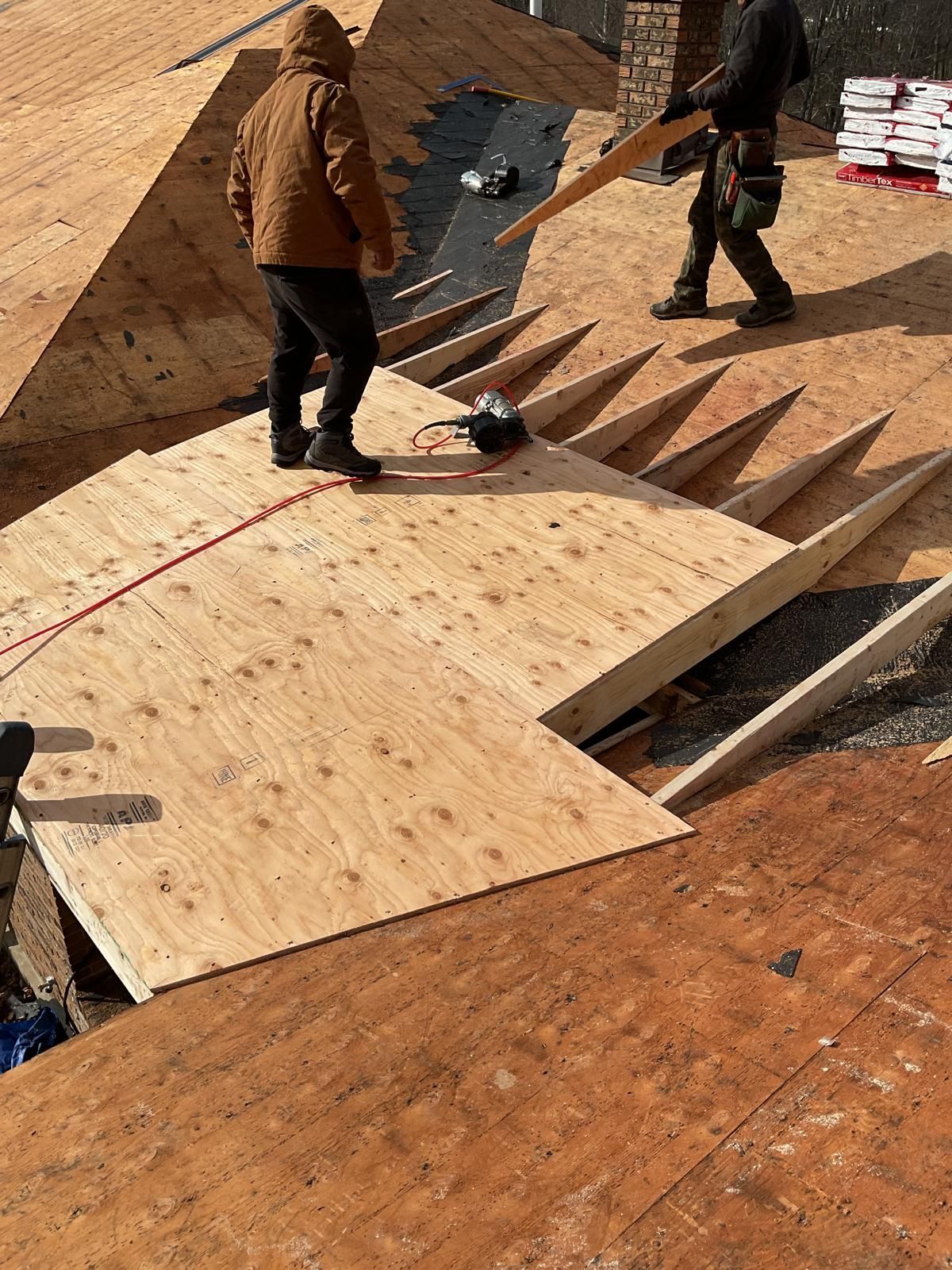 Two workers install plywood sheathing on a wooden roof frame at a construction site.