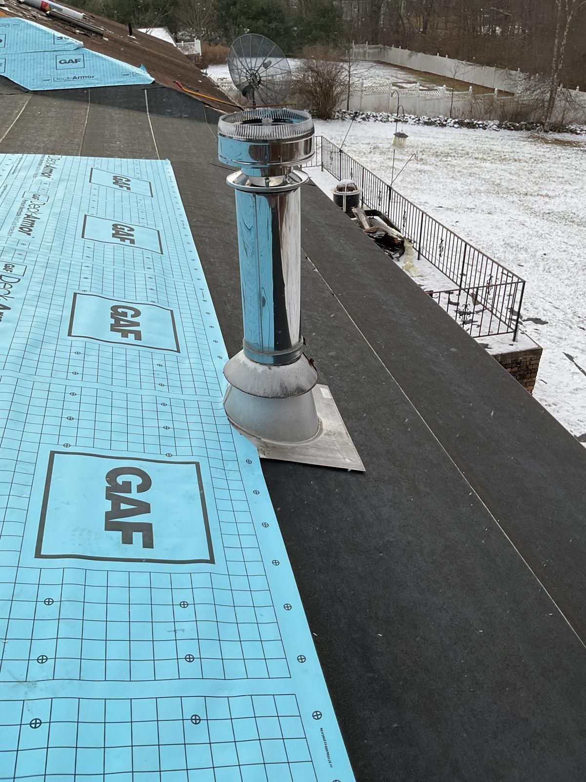 A stainless steel chimney vent pipe with a flashing base installed on a roof partially covered in blue GAF underlayment.
