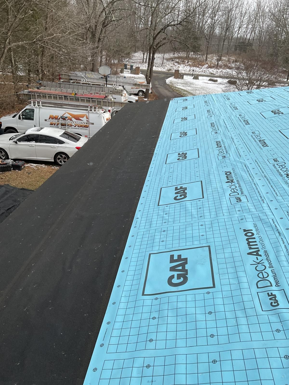 A roof under construction, featuring blue GAF Deck-Armor synthetic underlayment next to a strip of black roofing material.