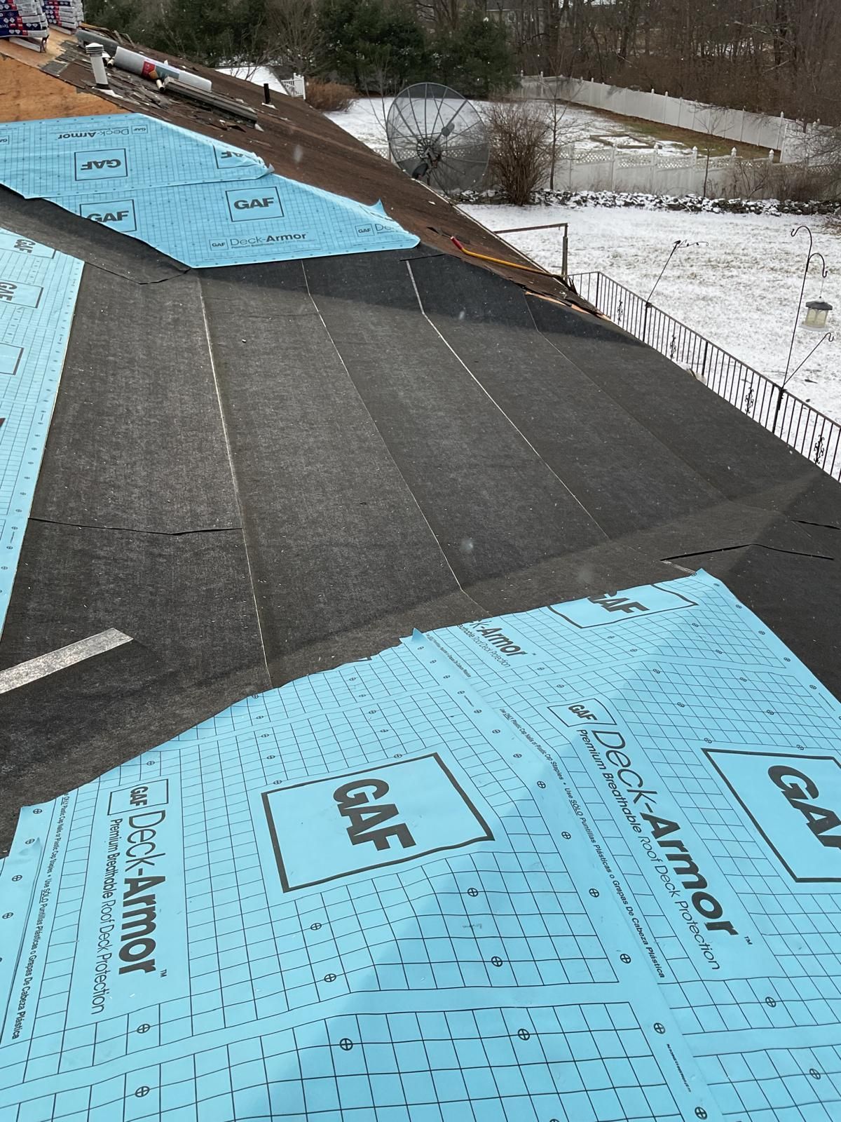 A high-angle view of a residential roof under construction, showing patches of black underlayment and blue GAF Deck-Armor.
