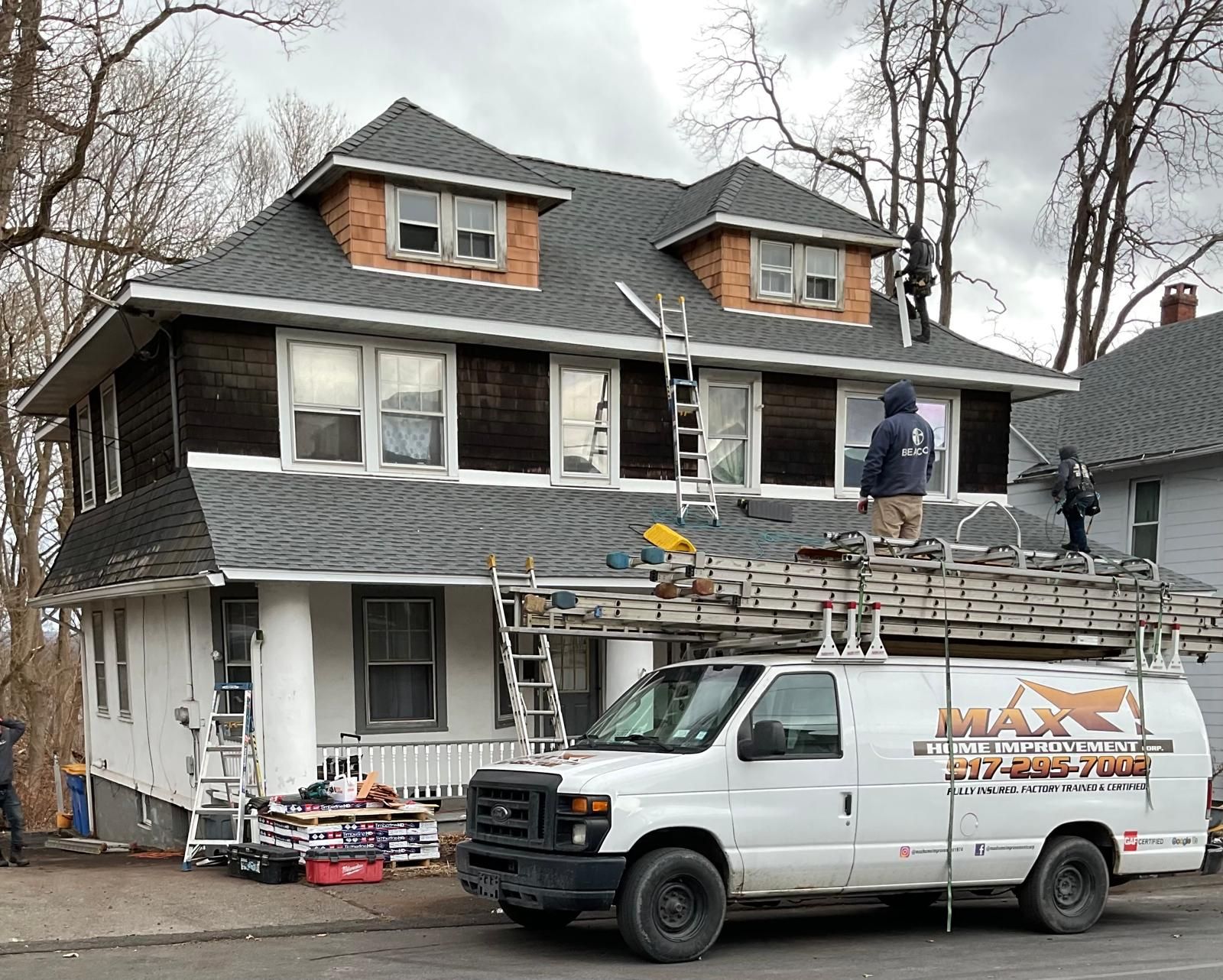 Workers on the roof of a two-story home, with a Max Construction van parked in front.