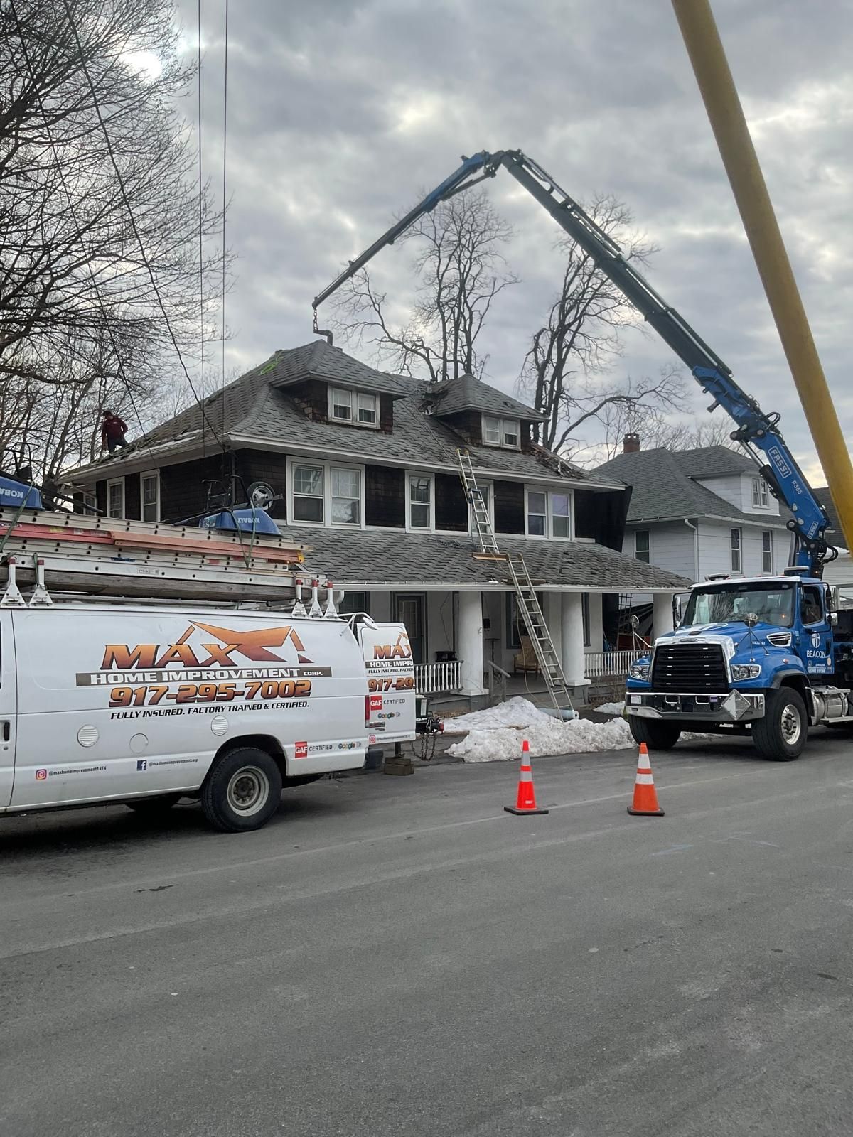 A large crane reaches over a two-story residential house during an exterior construction or renovation project.