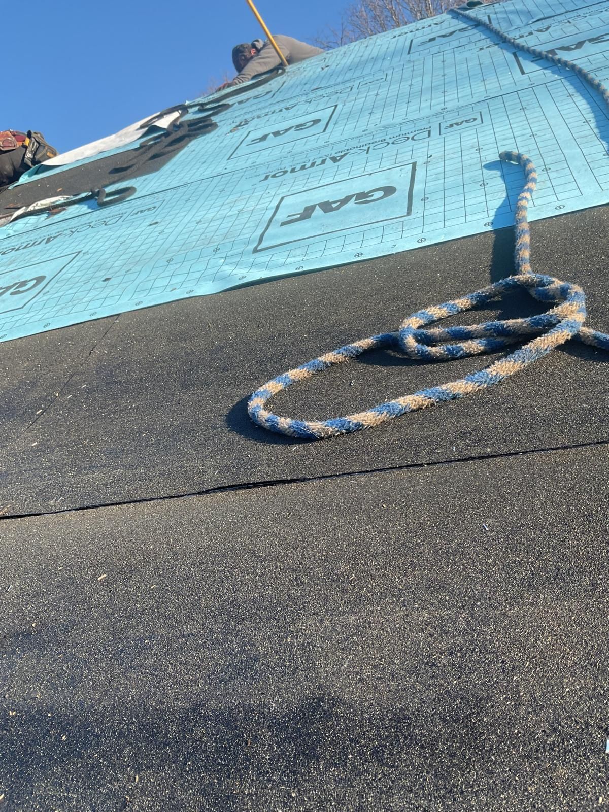 A blue synthetic roofing underlayment installed on a sloped roof with a coiled safety rope lying on the surface.