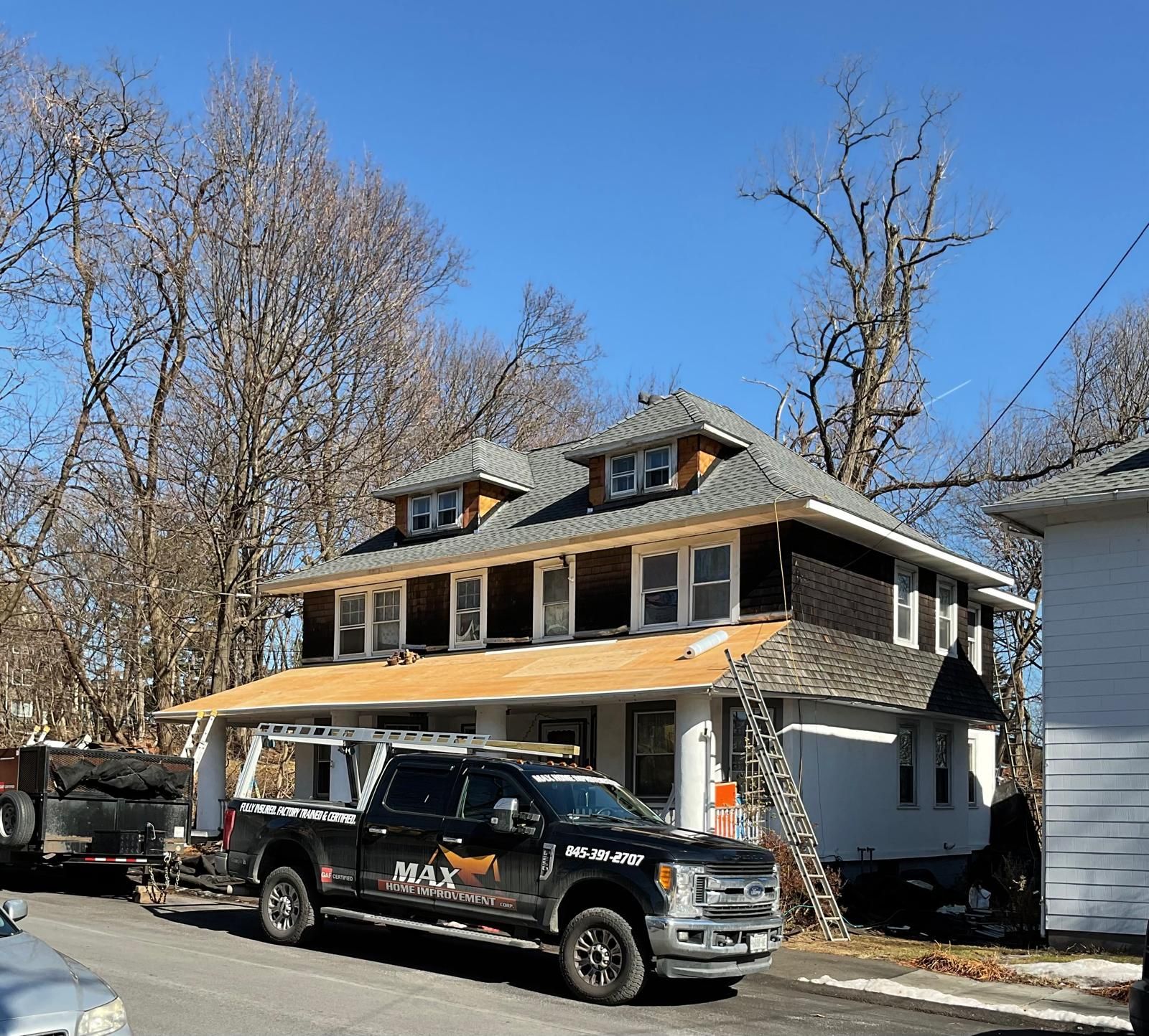 A black truck with a logo is parked in front of a white two-story house undergoing exterior renovations.