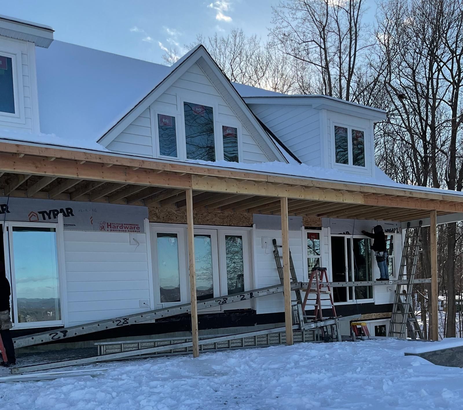 Construction crew working on the exterior of a white, partially finished house surrounded by snow.