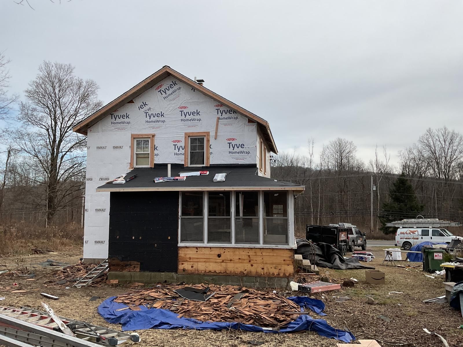 A two-story house under construction with white Tyvek wrapping on the upper level and an enclosed porch on the lower level.