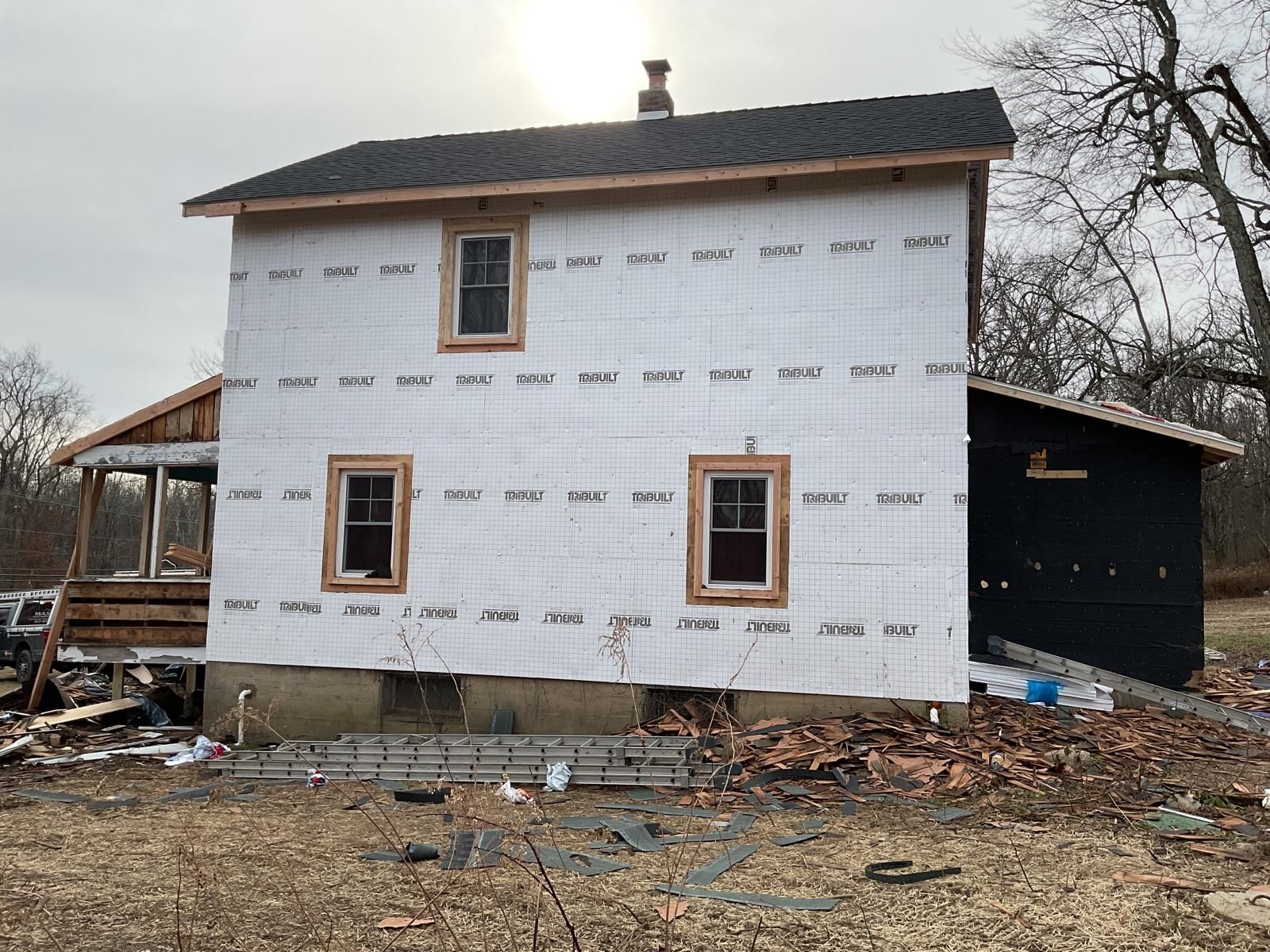 A house under renovation, featuring exposed white insulation panels and windows, set against a bare, wintry backdrop.