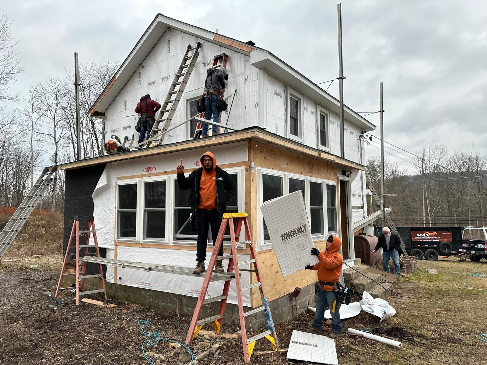 Construction workers in high-visibility gear install white insulation panels on the exterior of a two-story home.