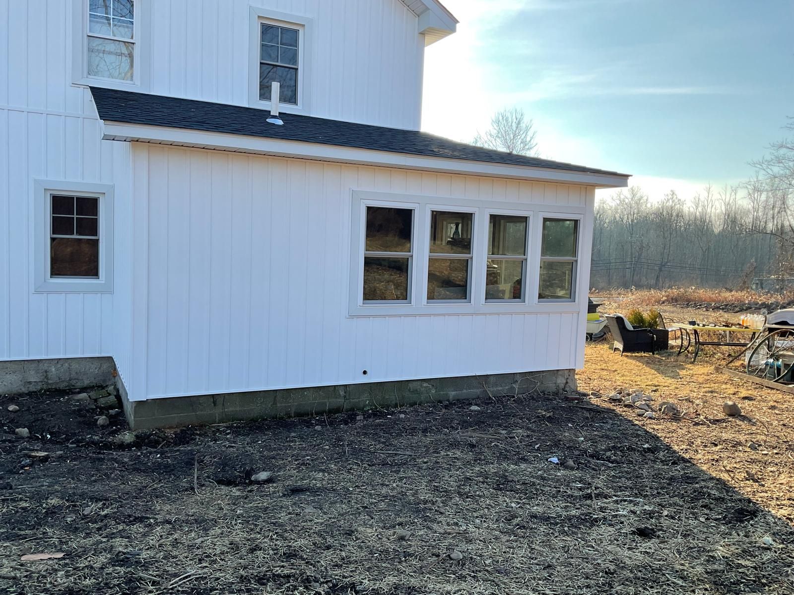 White house exterior with a sunroom addition and a dirt yard in a rural landscape under a clear sky.