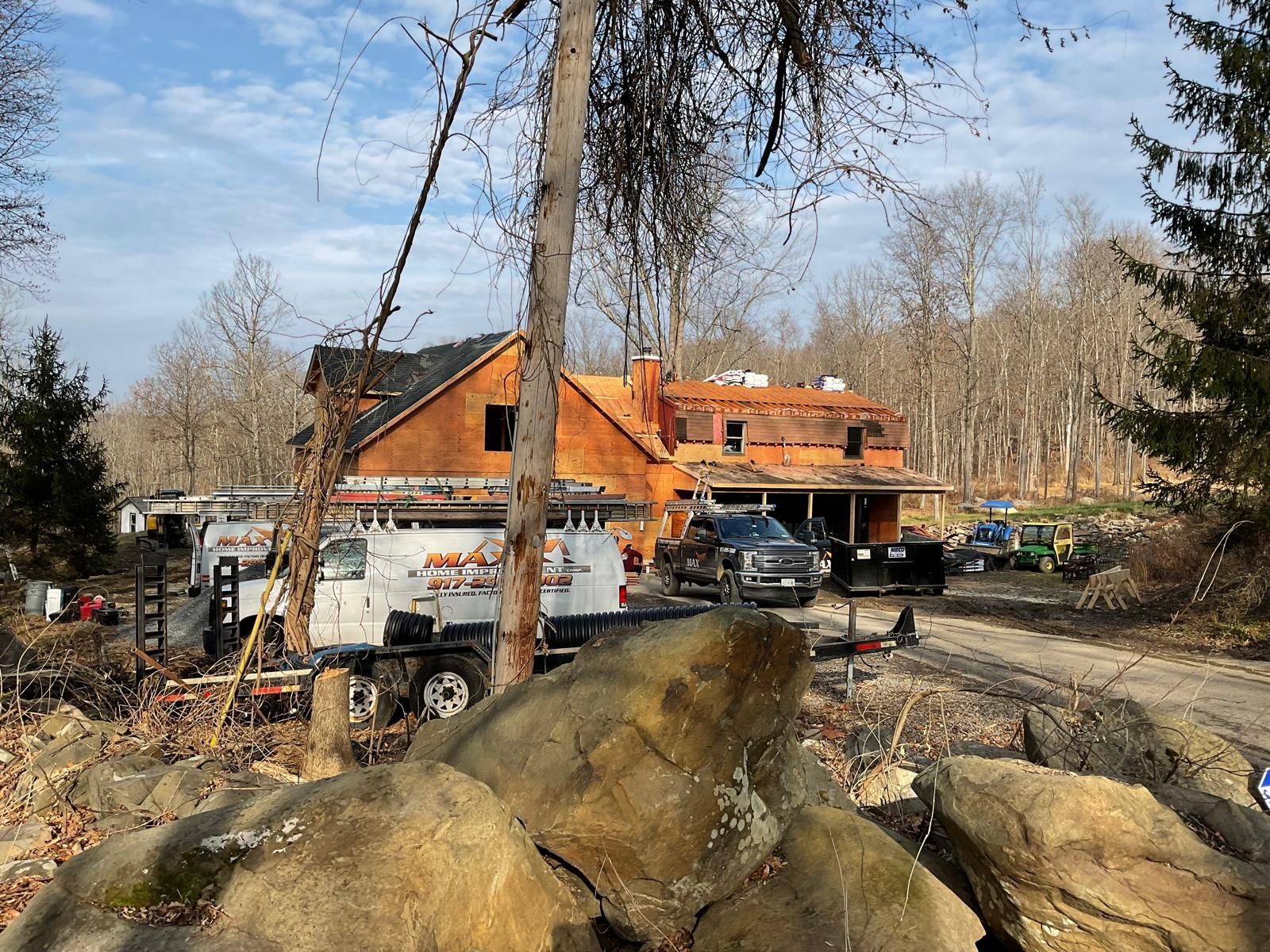A work truck parked in front of a house under renovation, surrounded by large rocks and bare trees under a blue sky.