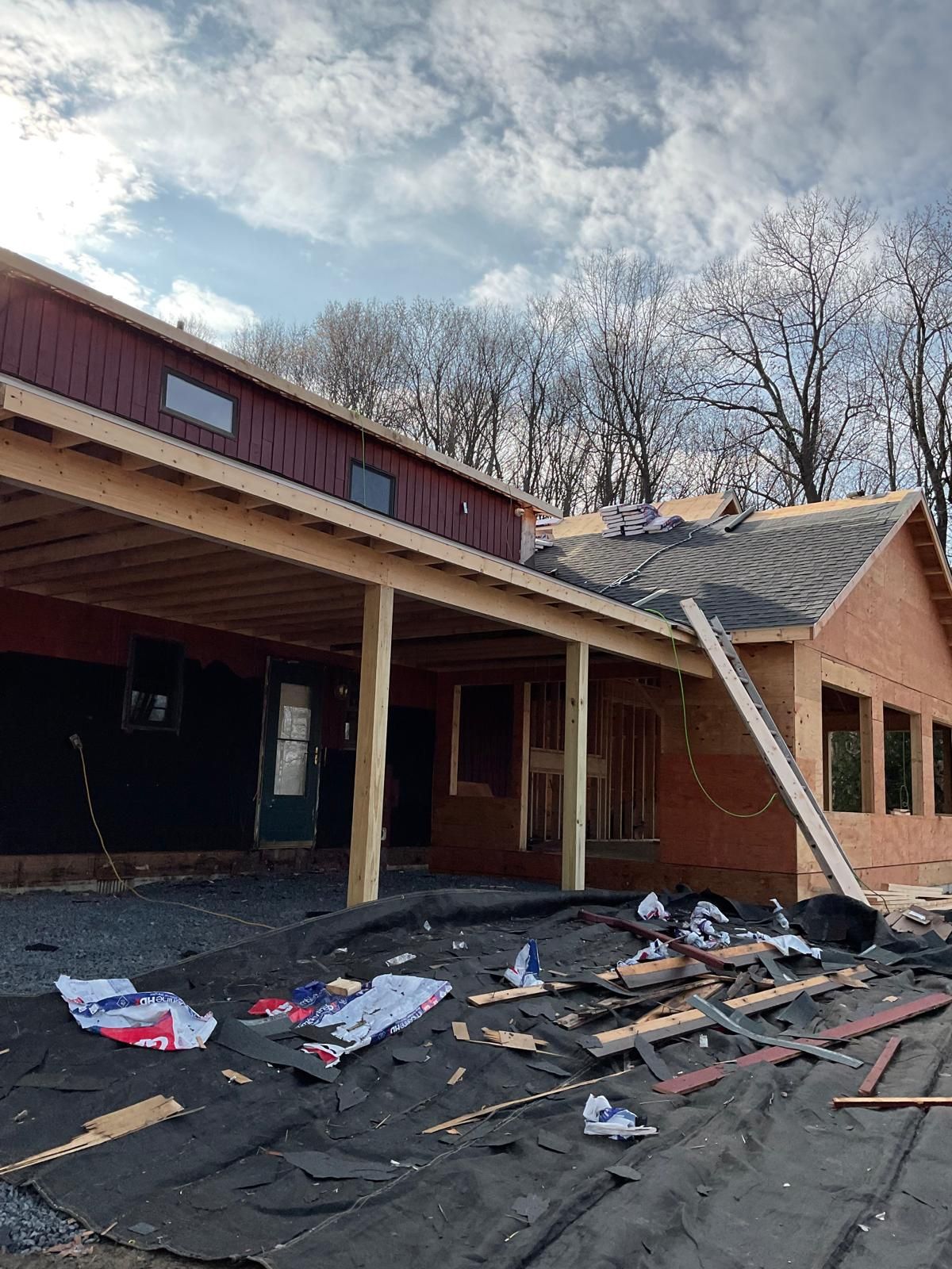 A house under construction with a metal roof, wooden porch frame, and debris scattered on the ground.