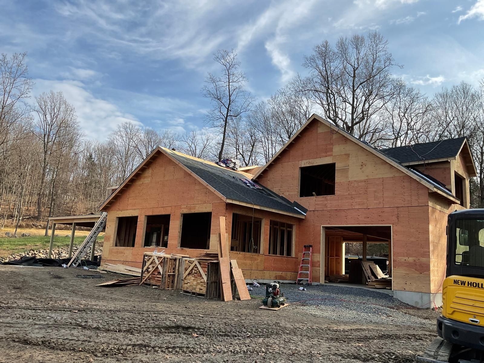 A new house under construction with brown wooden siding, a dark roof, and a partial garage opening on a dirt lot.