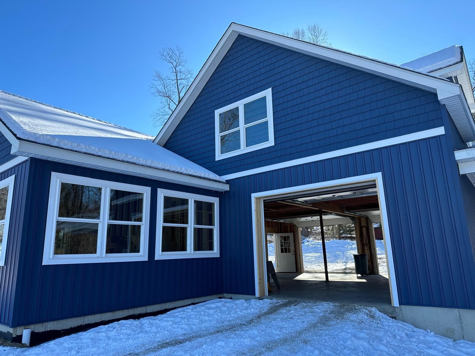 A blue house with white trim and windows features an open garage bay, with snow covering the surrounding ground.