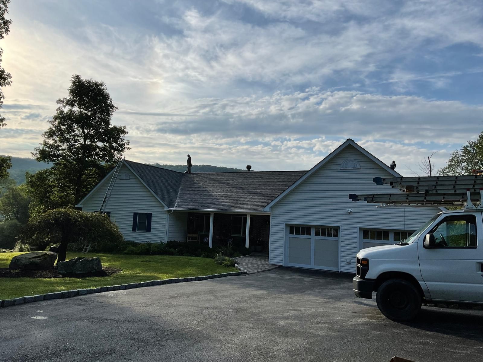 A white ranch-style house with a gray roof and a white work van parked in the driveway on a sunny day.