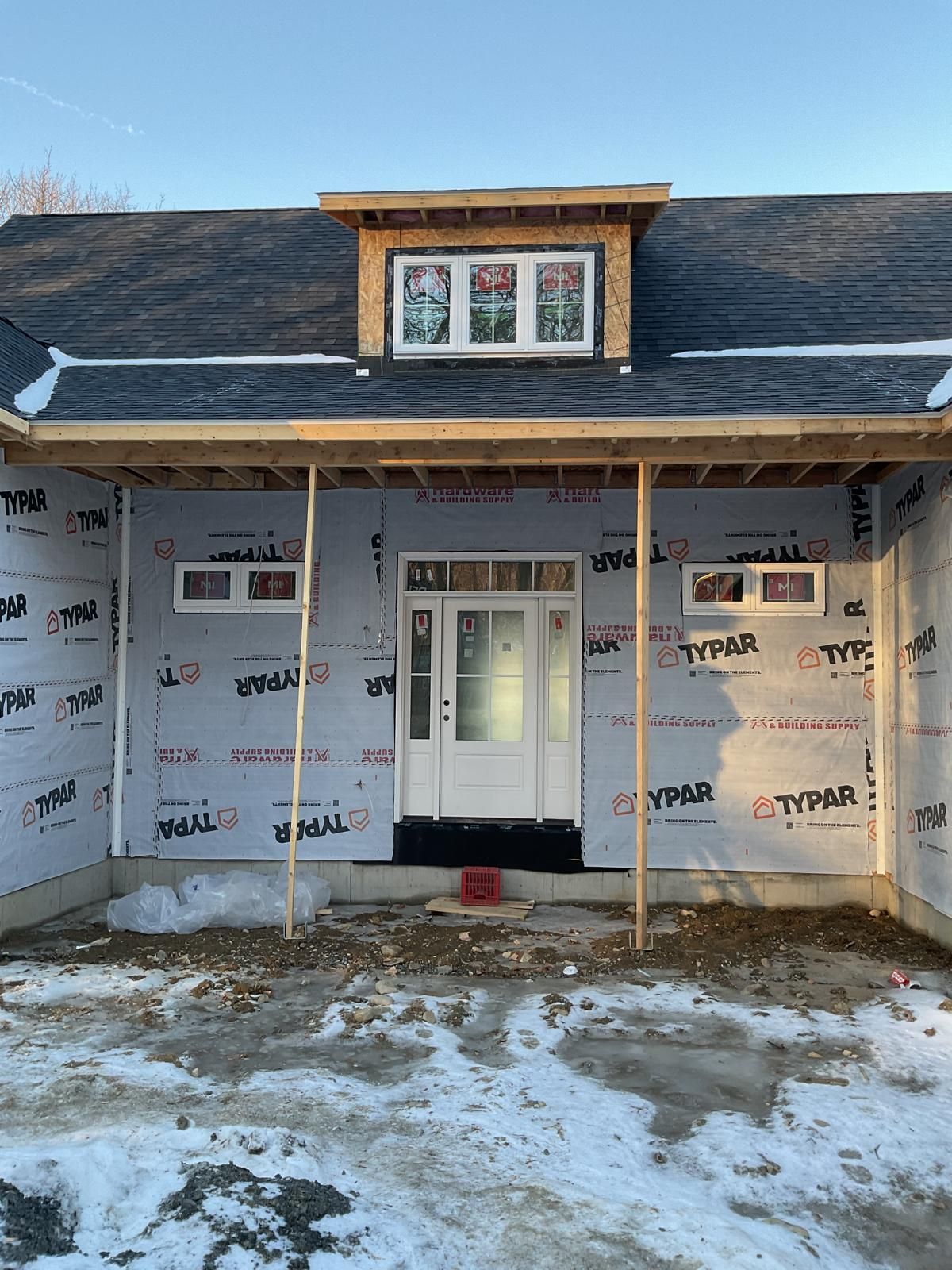 A new home under construction with a white front door, two small rectangular windows, and a dormer window above.