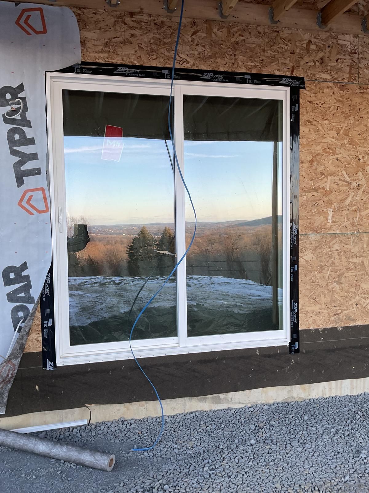 A white sliding window installed in a wood-framed wall under construction, with Typar house wrap on the left side.