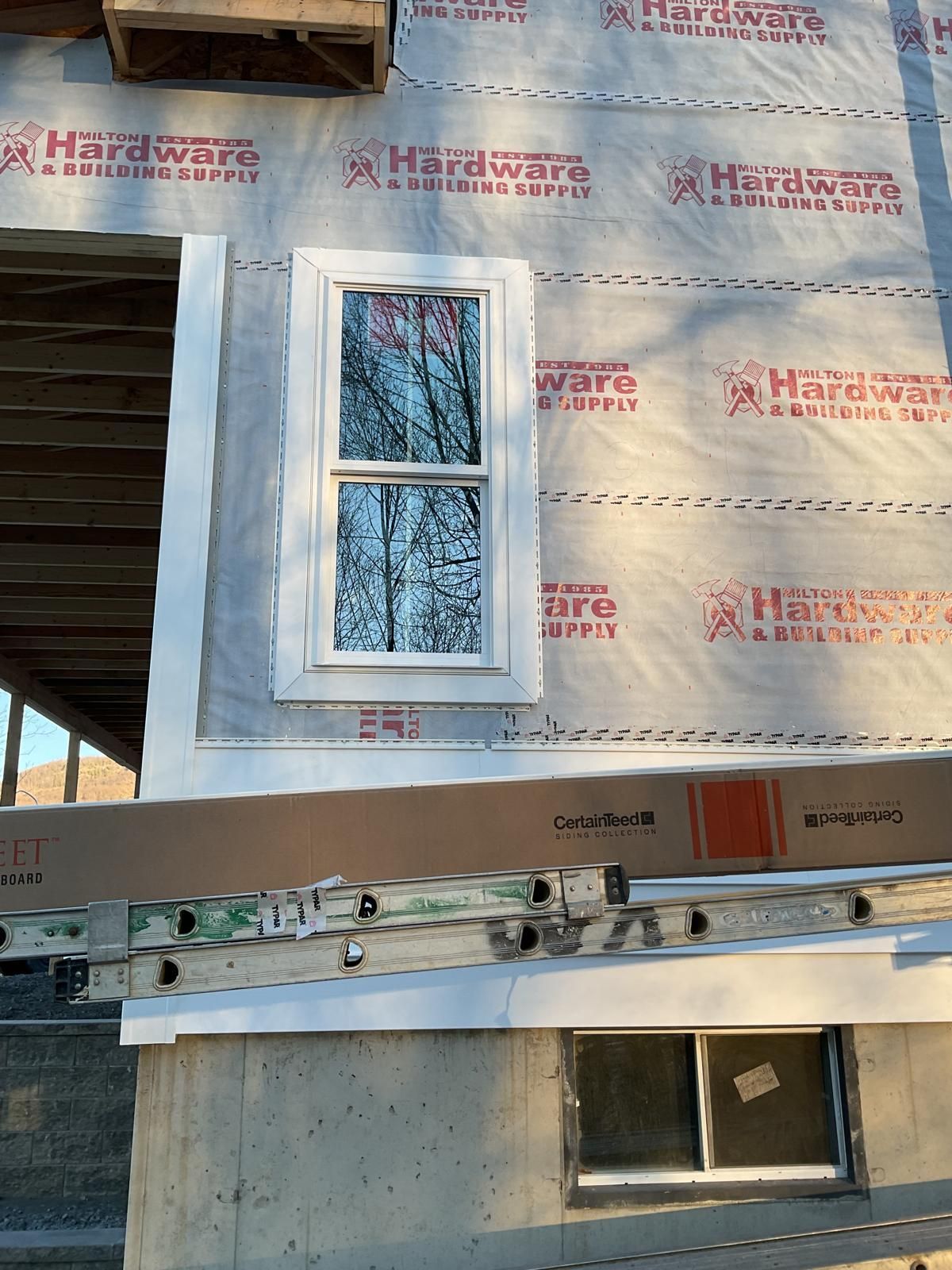 A window installed in a house under construction, featuring a white frame and surrounding weather-resistant barrier.